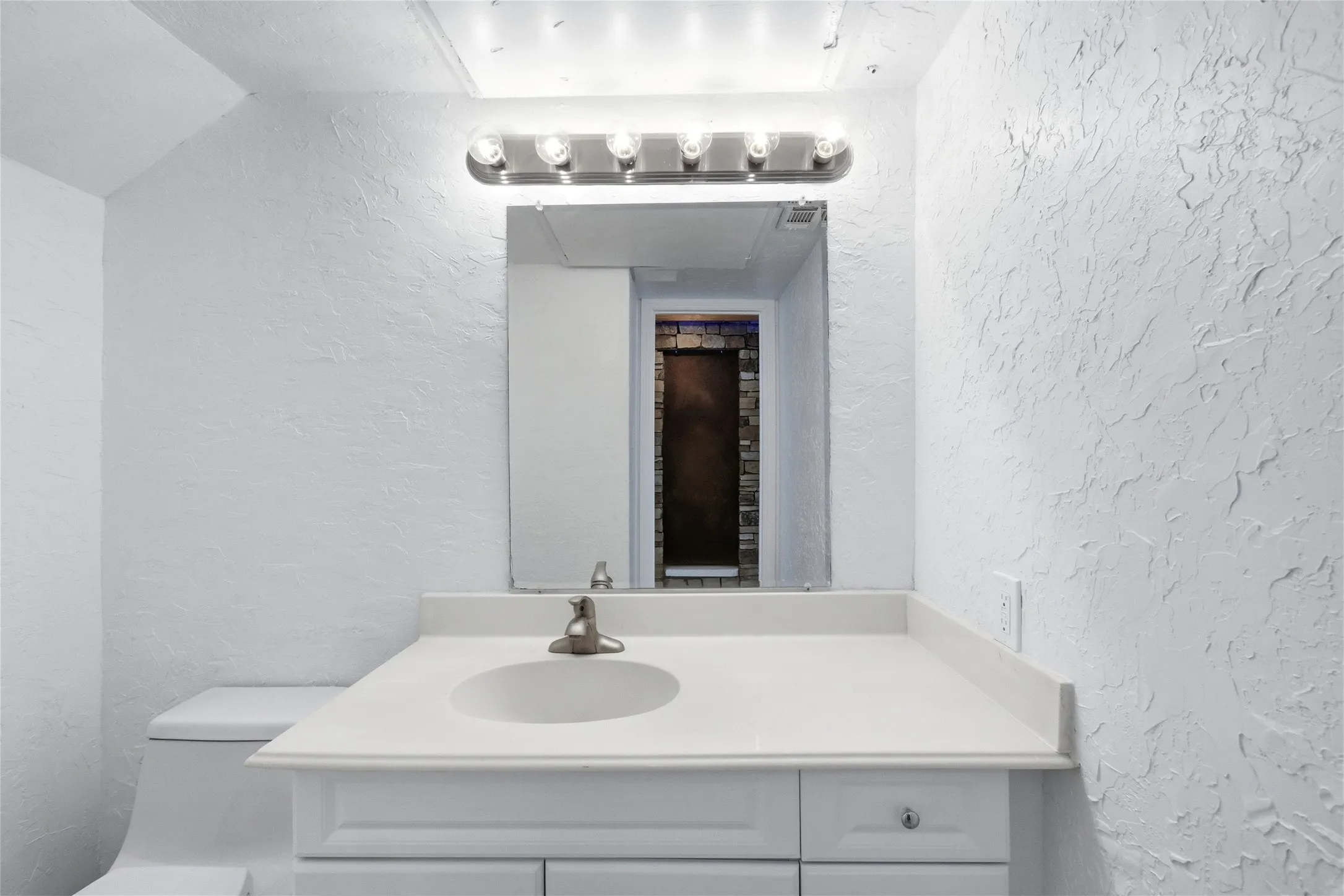 Vanity with an integrated sink, white countertop, brushed nickel faucet, and a wall-mounted light fixture