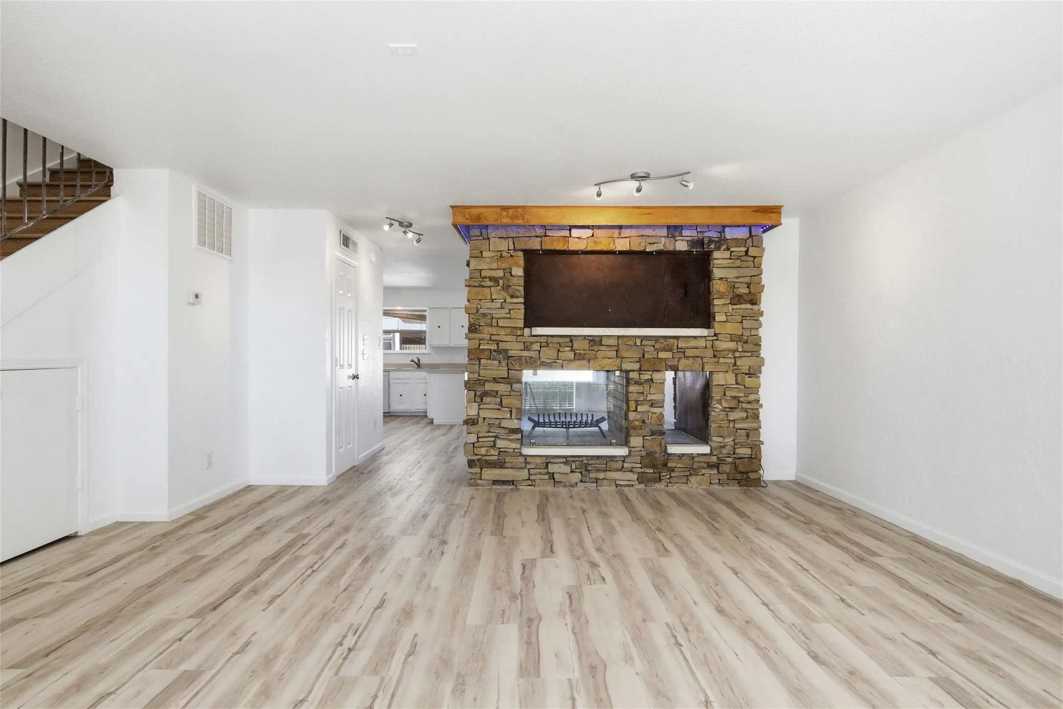 Wood-finish flooring throughout, featuring a stone-clad fireplace with a wood mantle and recessed lighting