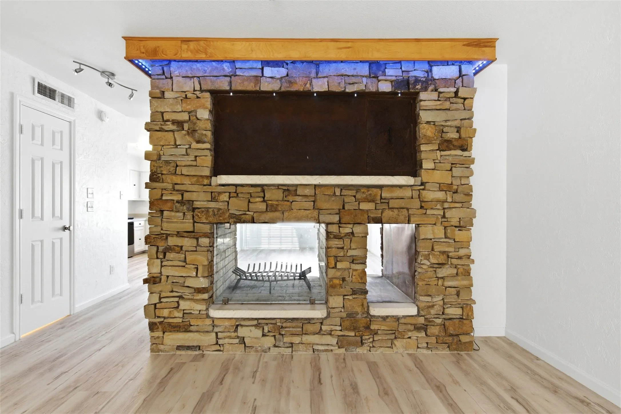 Stone-clad fireplace with a wood mantle featuring accent lighting, integrated media niche, and wood-finish flooring