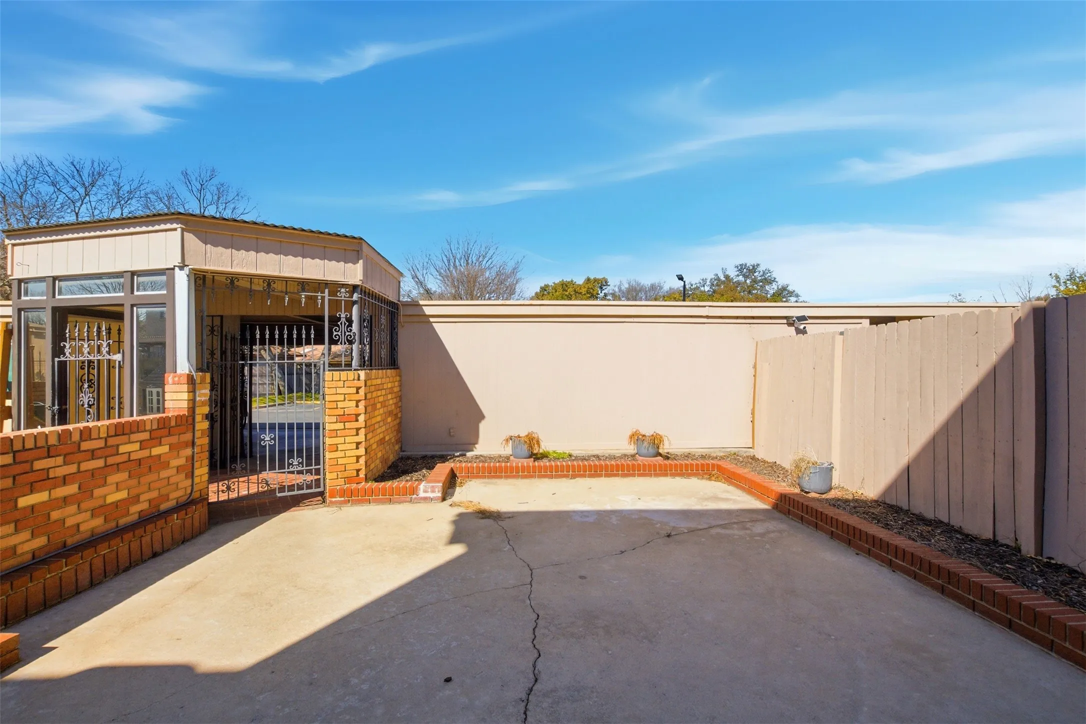 Concrete paving with brick border detailing, featuring a security gate, and an enclosed sunroom with window panels