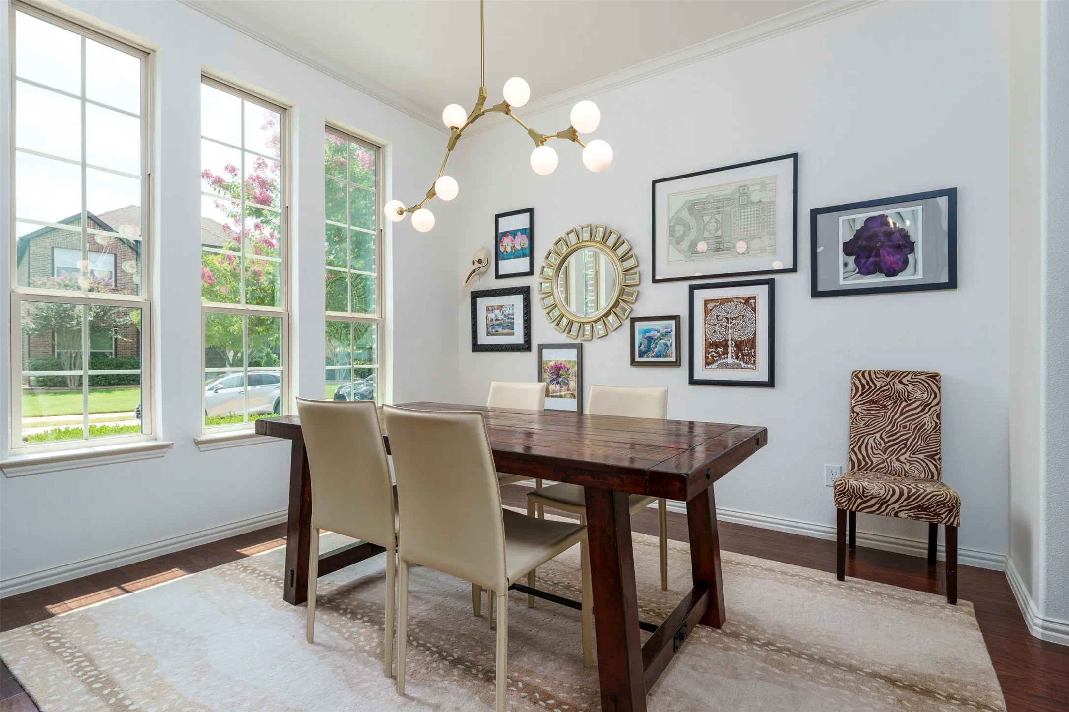 Spacious, light-filled dining room features a wall of oversized windows, crisp light paint, rich wood floors, and a striking modern Sputnik-style chandelier. The open, airy design creates an inviting setting for everyday meals and elegant entertaining, while abundant natural light highlights the room's warm architectural details and generous proportion