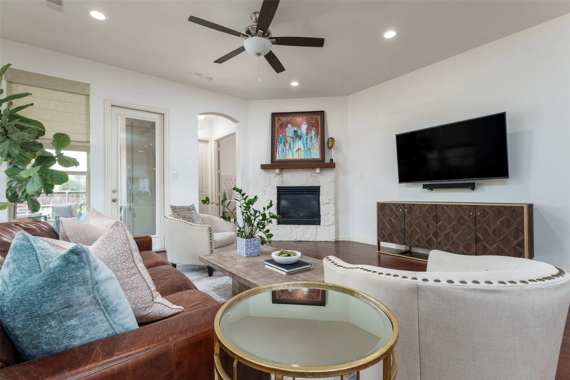Spacious living room centers around a painted brick gas-log fireplace, creating a warm and inviting focal point. Recent interior paint, rich wood floors, recessed can lighting, and a neutral color palette provide a fresh, updated feel. The generous layout offers plenty of space for comfortable seating and entertaining, with an open flow that connects seamlessly to the home's main living areas.