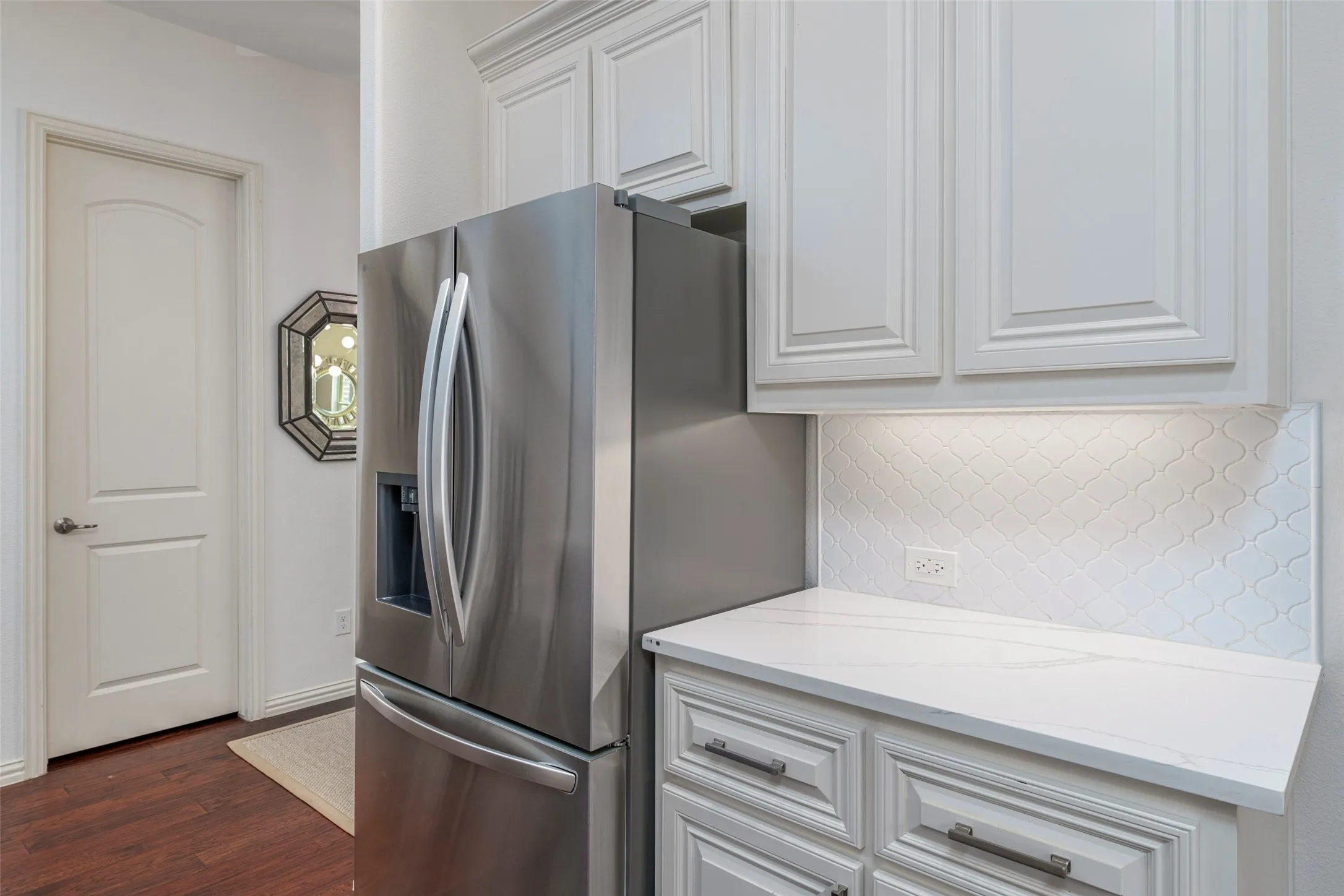 Updated kitchen offers a stylish combination of white shaker cabinetry, white quartz countertops, and stainless steel appliances. Generous countertop workspace provides excellent room for meal preparation and entertaining, while the decorative tile backsplash adds a fresh, contemporary touch. Rich wood floors complement the bright finishes, creating a clean, functional, and inviting kitchen.