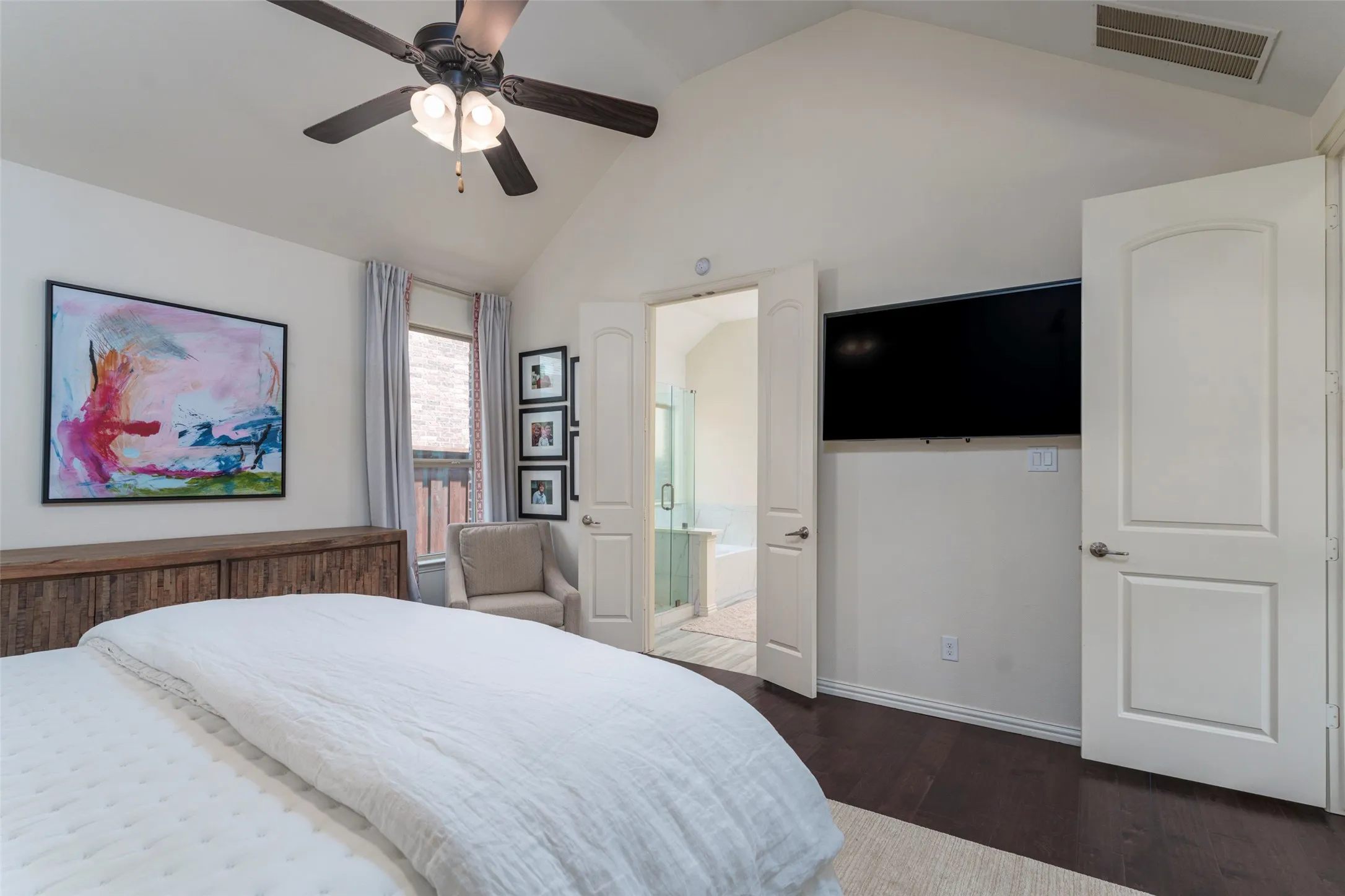 Spacious downstairs primary bedroom featuring high ceilings, rich wood floors, and a ceiling fan for year-round comfort. Dedicated wiring for a wall-mounted flat-screen TV creates a clean, functional entertainment setup, while the generous floor plan offers plenty of space for a king-size bed and additional furnishings.
