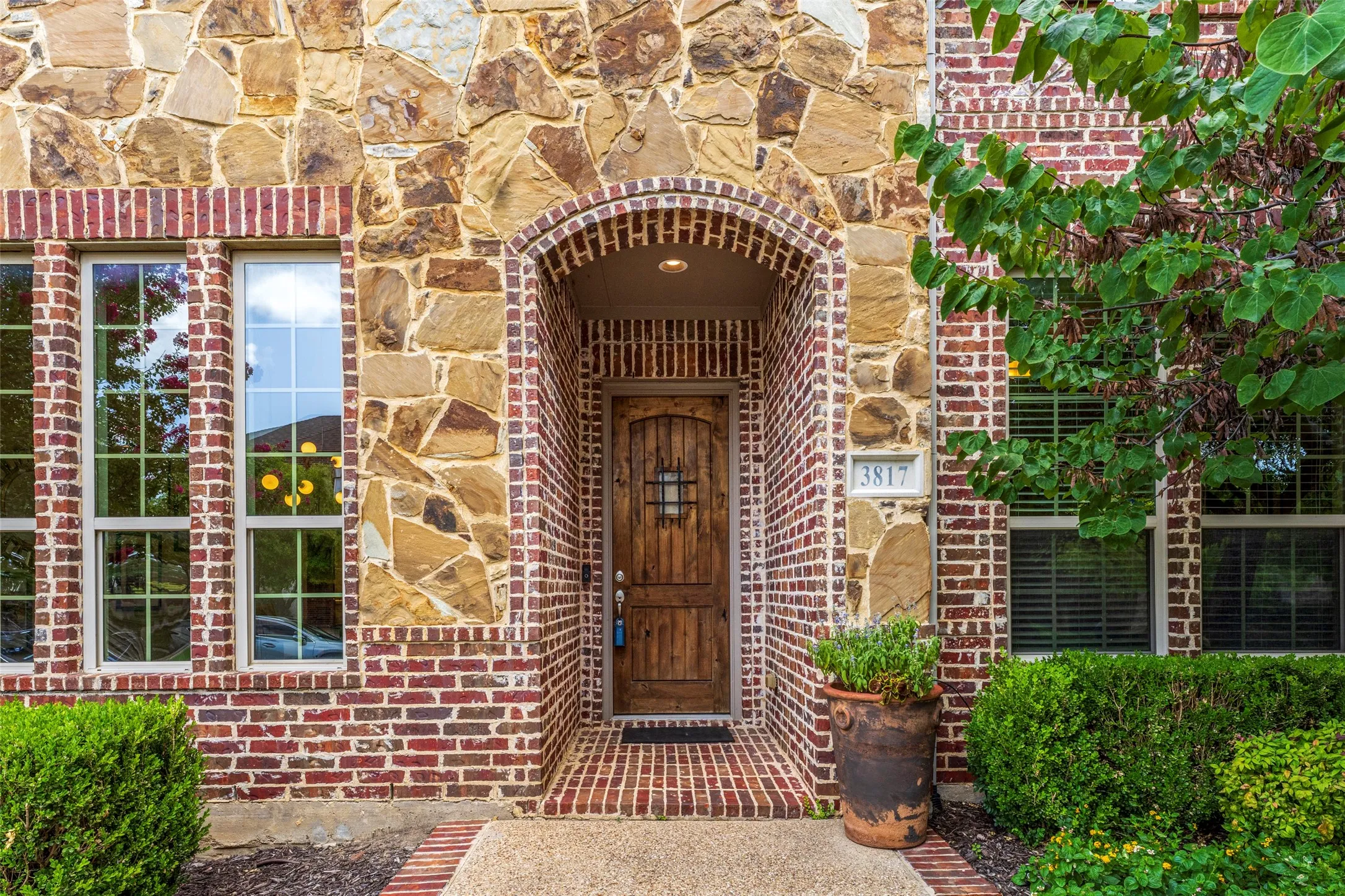 Stunning entry in the Viridian master-planned community of Arlington, TX, showcasing beautiful natural stone and brick accents, a substantial heavy wood front door, arched brick detailing, and a welcoming brick-lined entryway. Meticulously landscaped beds frame the inviting entrance and enhance the home's distinctive curb appeal. Enjoy the exceptional Viridian lifestyle with scenic parks, a private community lake, walking trails, and multiple resort-style community pools.