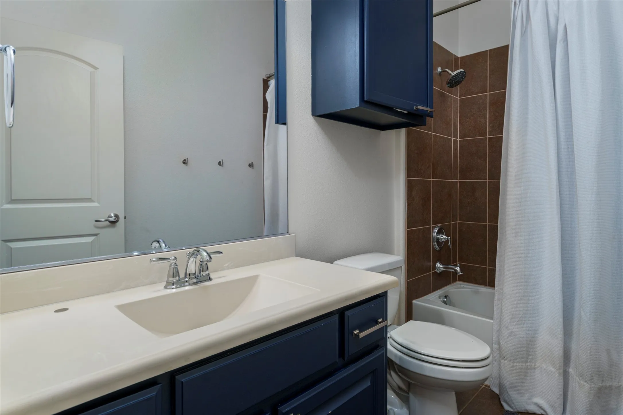 Upstairs Guest Bathroom: Functional and inviting guest bath featuring a tub-shower combination, neutral tile surround and flooring, generous vanity storage, and convenient additional storage above the toilet. A practical layout designed for family and overnight guests.