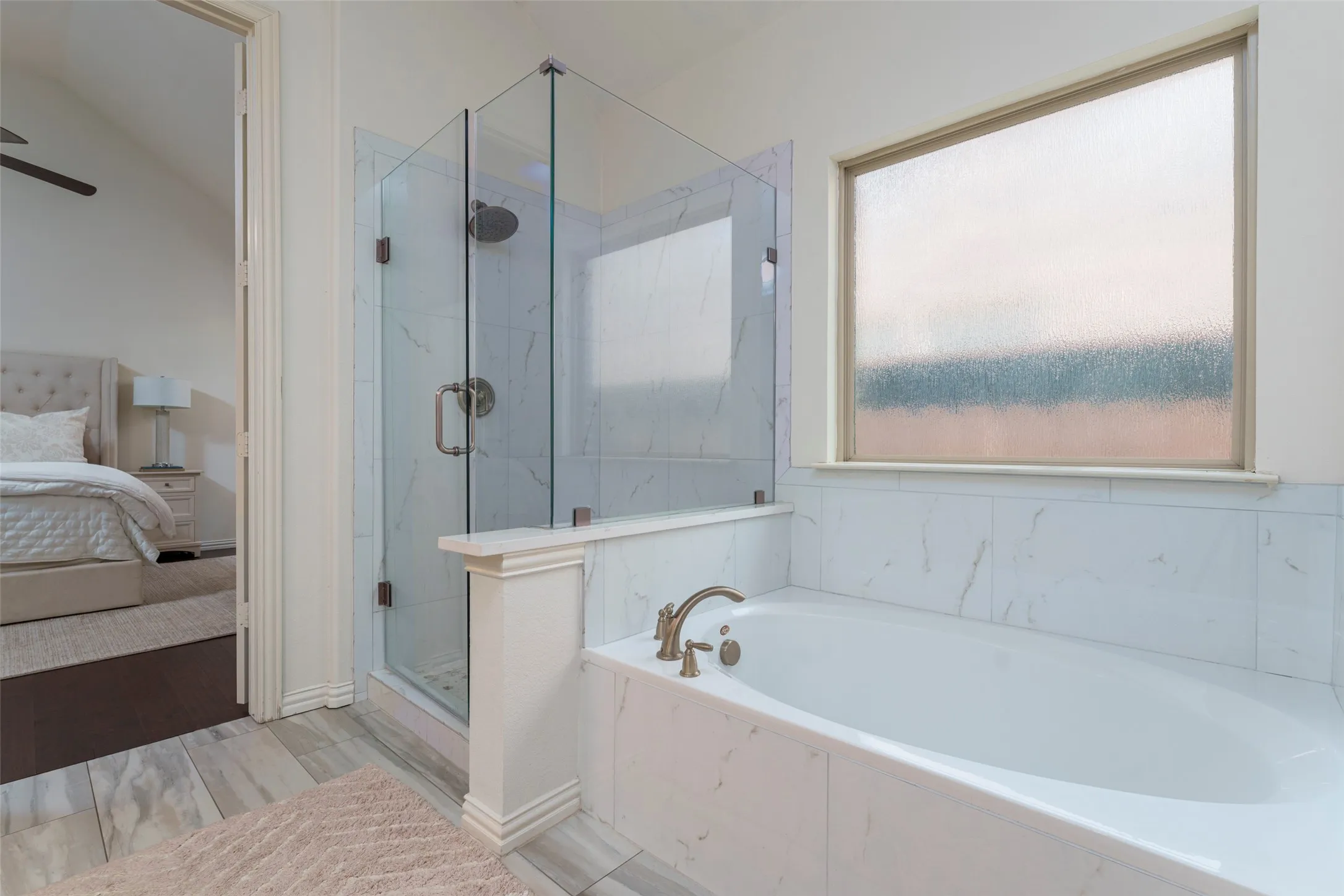 Relax and unwind in the spacious primary bathroom featuring a deep soaking tub—perfect for relaxing after a long day. A seamless glass-enclosed shower with updated plumbing fixtures adds a modern touch, while the frosted privacy window fills the space with natural light. Neutral tile flooring and bright finishes create a clean, spa-like retreat.