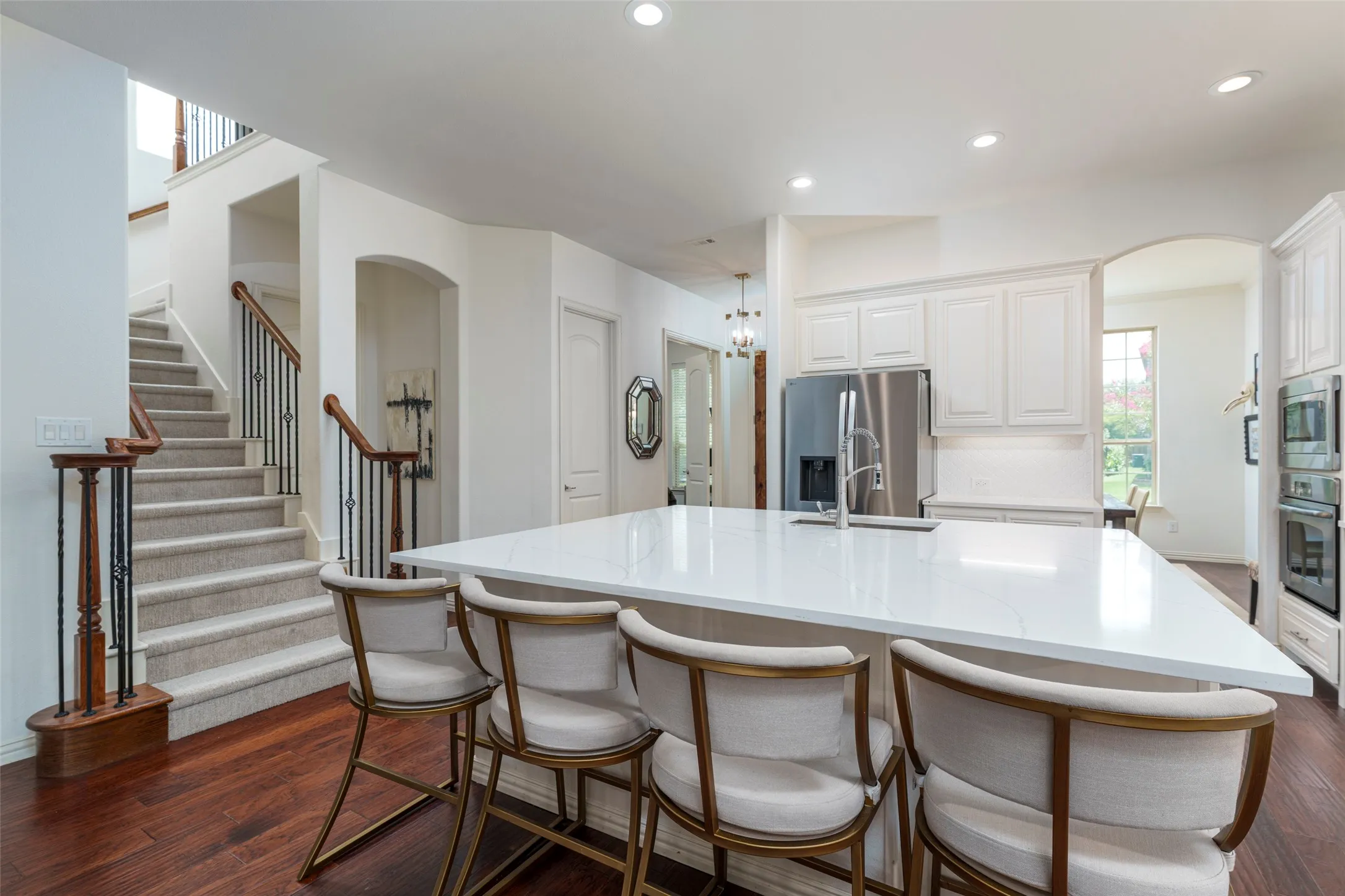 Recently updated open-concept kitchen showcases an expansive squared-off center island with generous workspace and room for four barstools, making it the perfect gathering spot for entertaining. White shaker cabinetry, white quartz countertops, under-cabinet lighting, and stainless steel appliances create a bright, modern look. Features include a gas cooktop, convection oven, built-in microwave, and refrigerator available for purchase. Rich wood floors and open sightlines provide seamless flow to the dining and living areas.