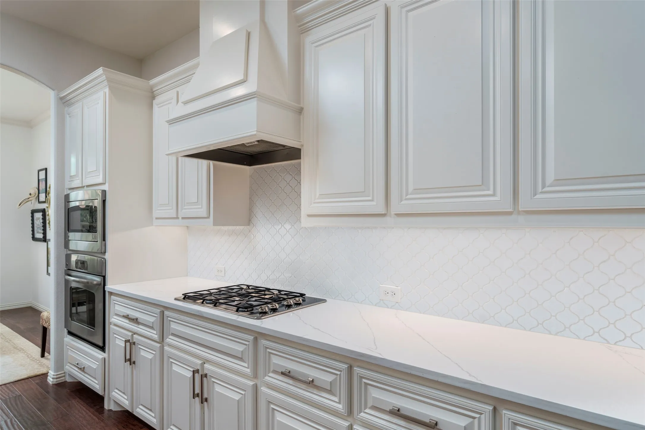 Beautifully updated kitchen showcases abundant quartz countertop workspace, providing plenty of room for meal preparation and entertaining. Crisp white shaker cabinetry offers ample storage, while the custom wood-trimmed vent hood adds architectural character above the gas cooktop. A stylish patterned tile backsplash complements the bright, timeless design, creating a functional and inviting updated kitchen in Viridian, Arlington, TX.