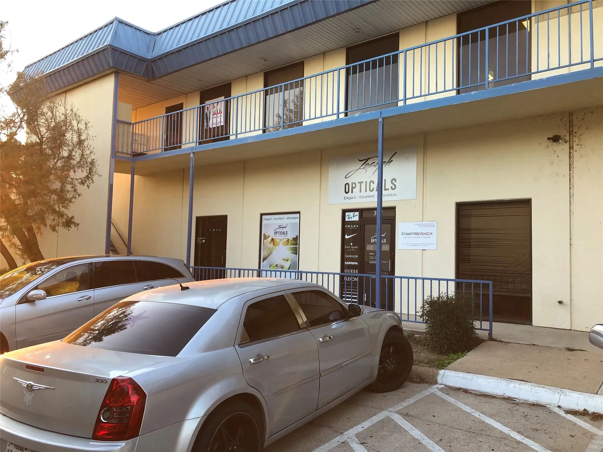 Two-story commercial building featuring light-colored exterior walls, a blue metal roof, and a second-story balcony with metal railings
