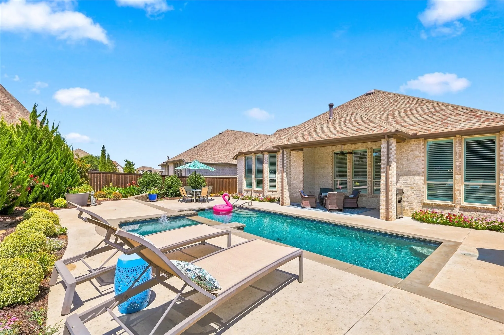Backyard oasis featuring a rectangular swimming pool, integrated spa, covered patio, and mature landscaping