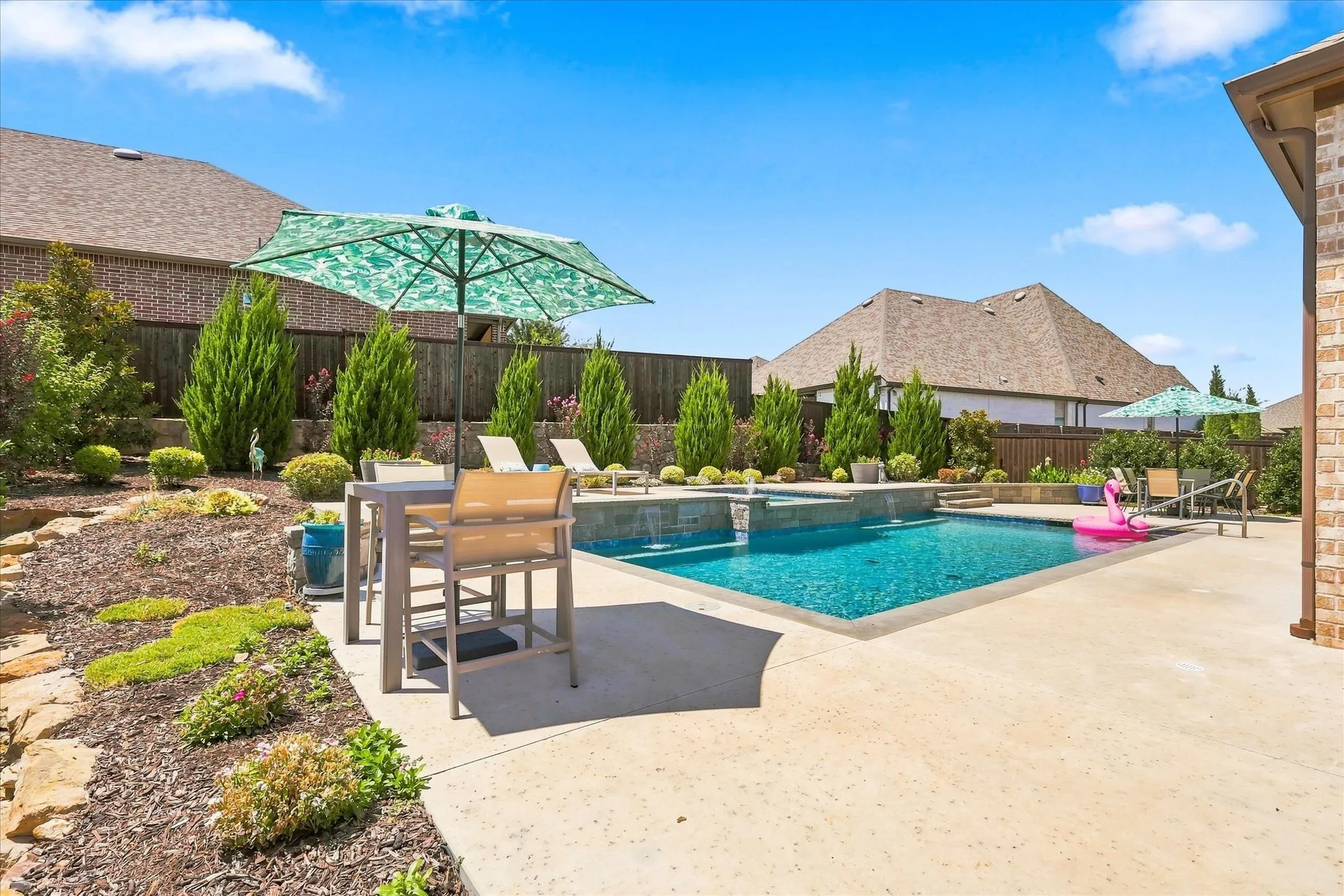 Backyard featuring a rectangular swimming pool with integrated water features, expansive concrete decking, and tiered landscaping
