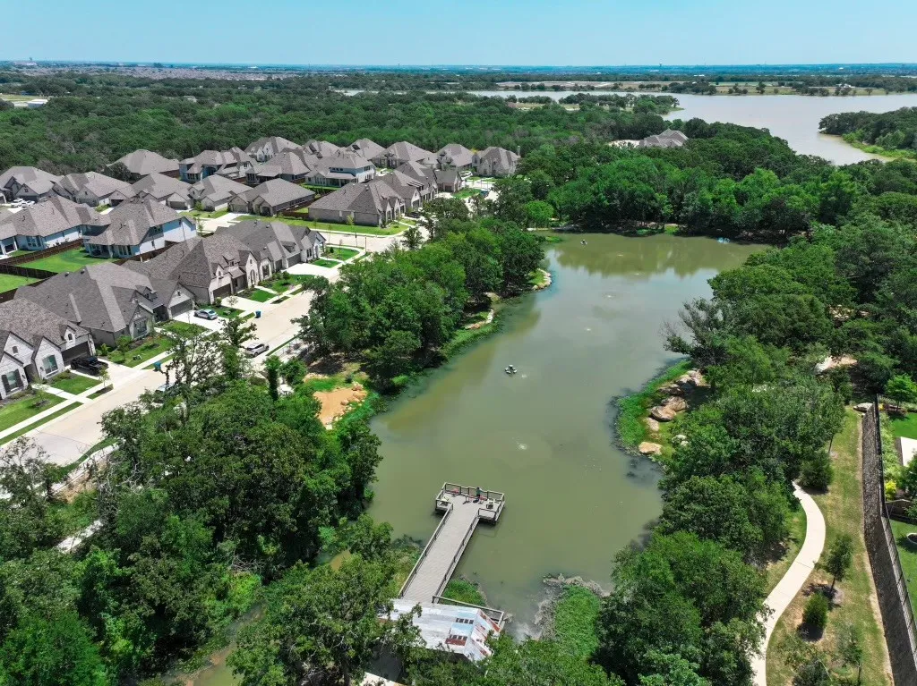Residential community featuring a private lake with a dock, surrounding green spaces, and a paved walking path