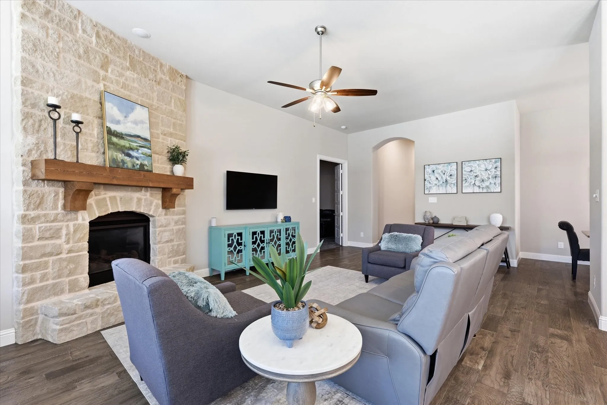 Stone-clad fireplace with a wood mantel, wood-finish flooring, recessed lighting, and a ceiling fan