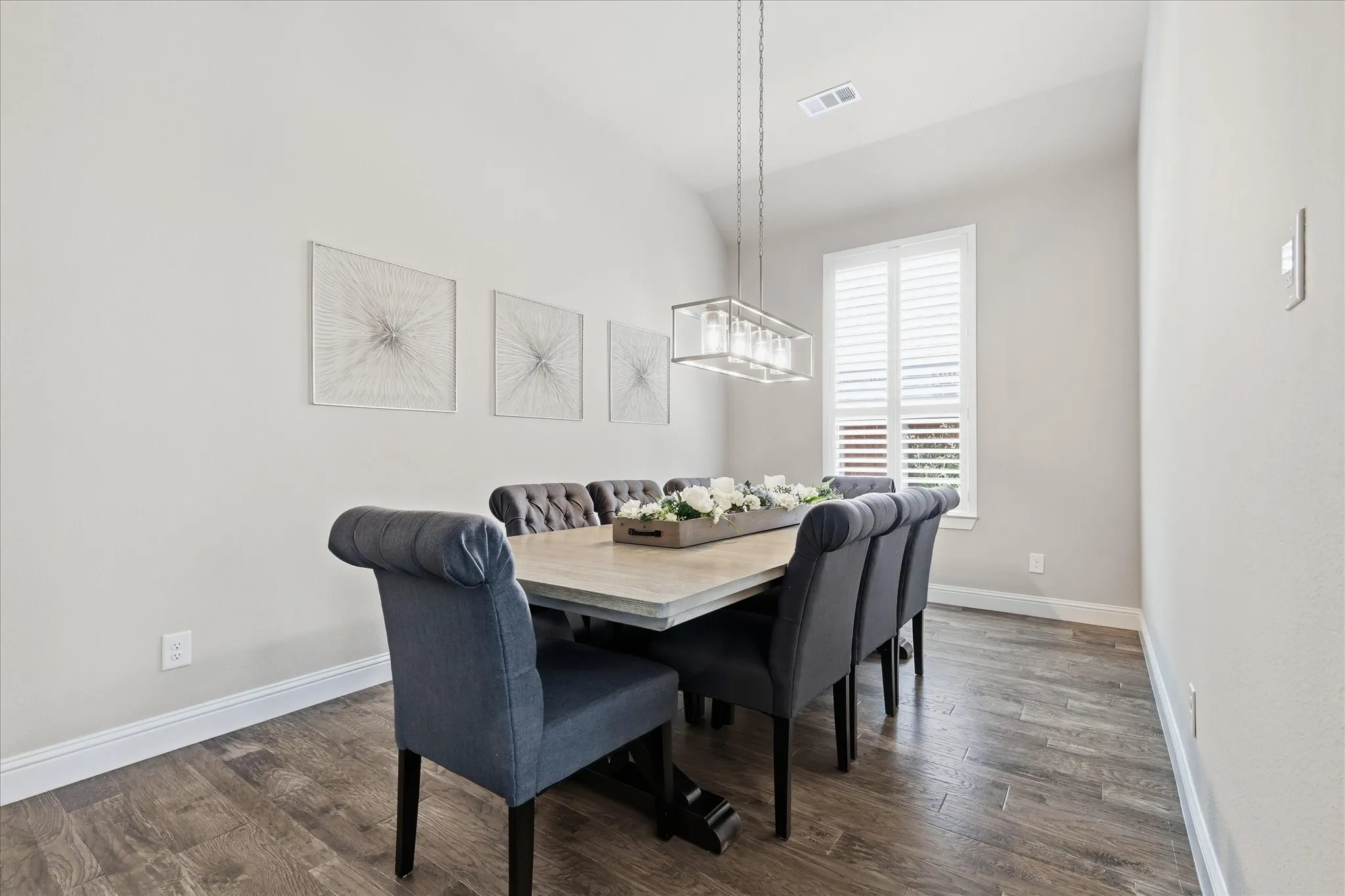 Dining area featuring wood-finish flooring, a rectangular linear chandelier, and a window with white louvered shutters