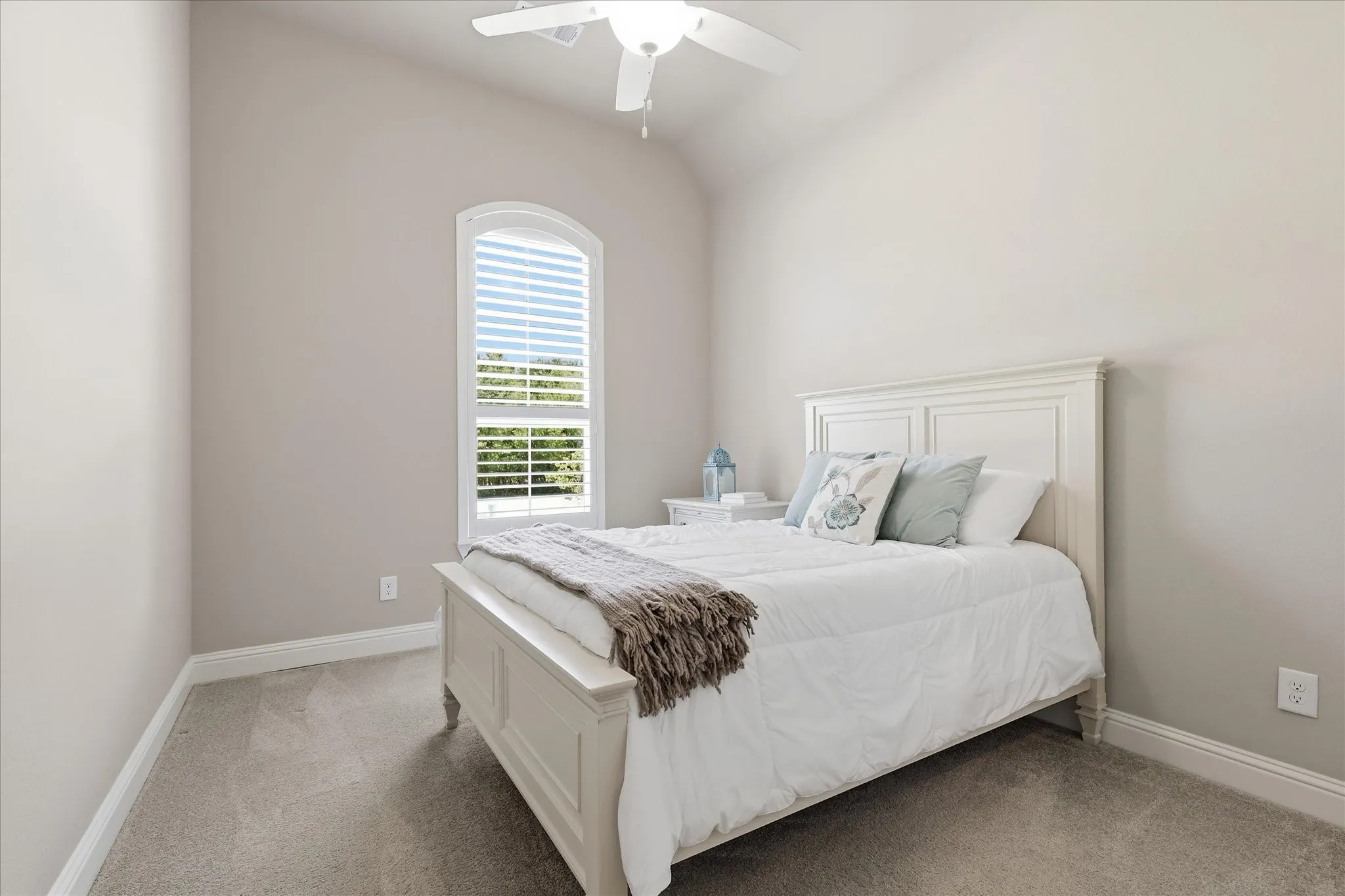 Vaulted ceiling with a ceiling fan, arched window with horizontal blinds, neutral wall paint, and gray carpet flooring