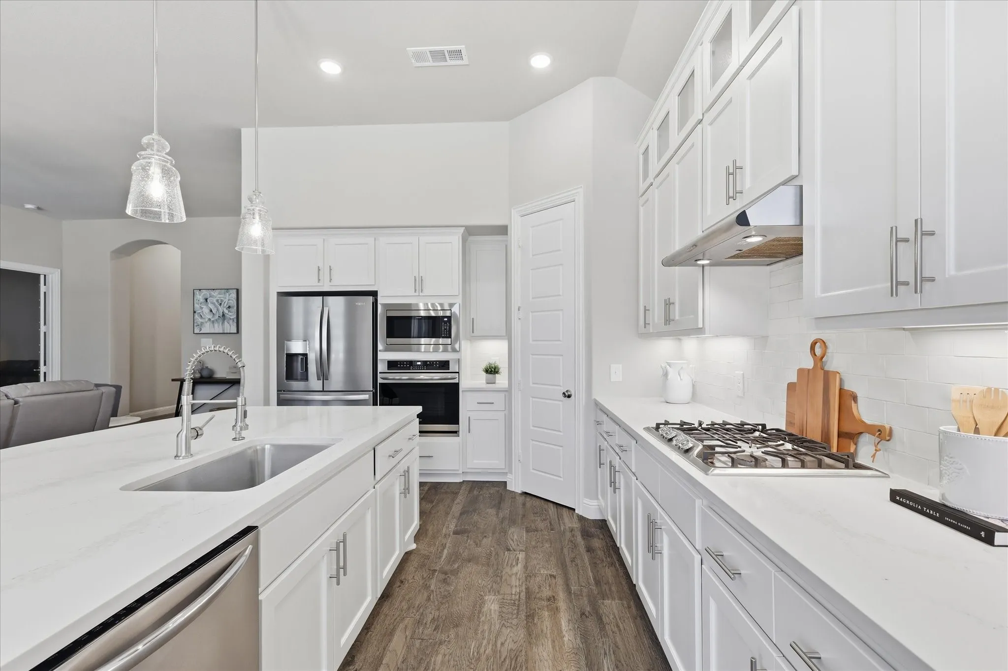 White cabinetry, stainless steel appliances, wood-finish flooring, recessed lighting, and a kitchen island with sink