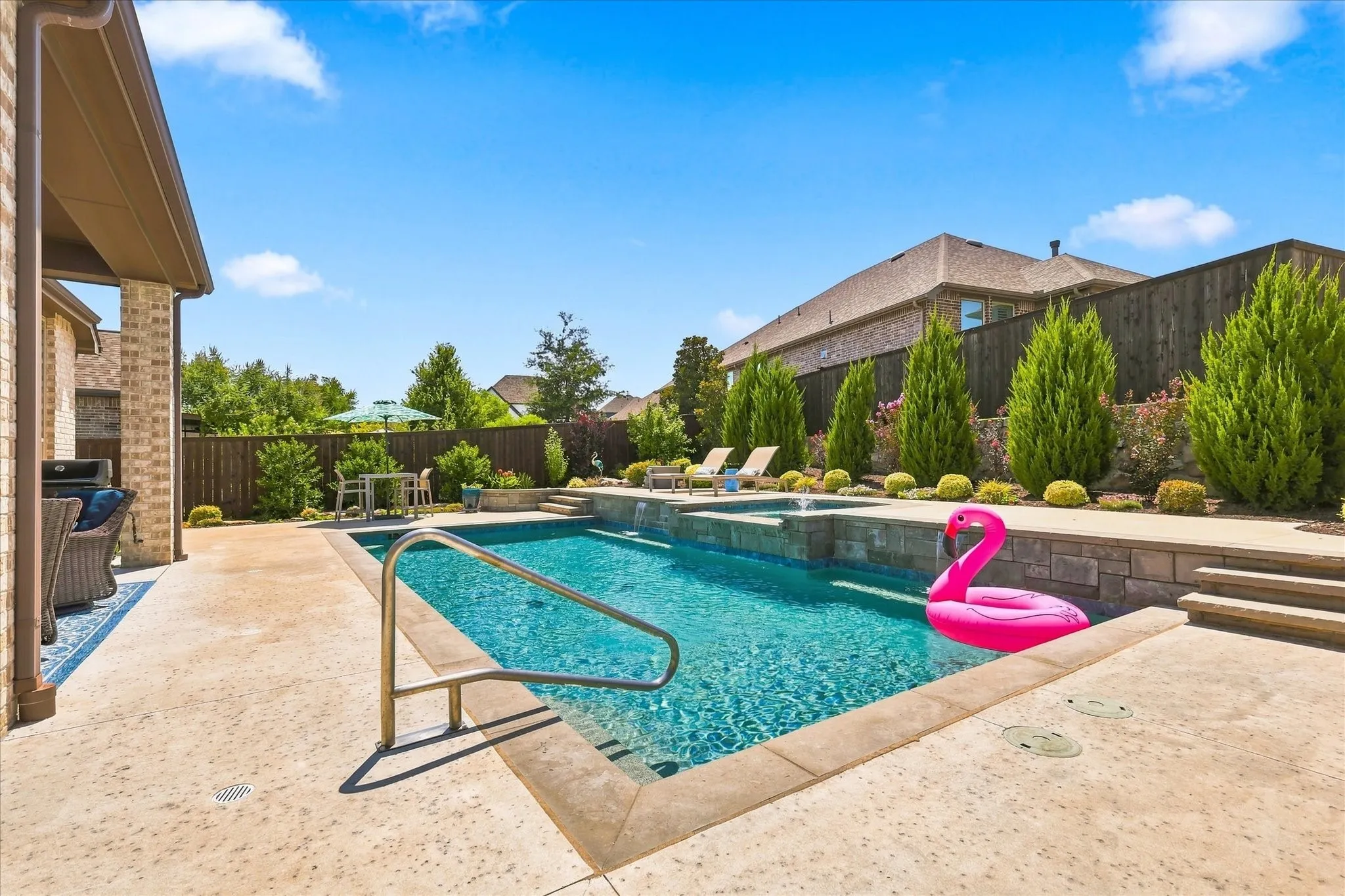 Private swimming pool with an integrated spa, expansive concrete patio, and stone-faced retaining walls