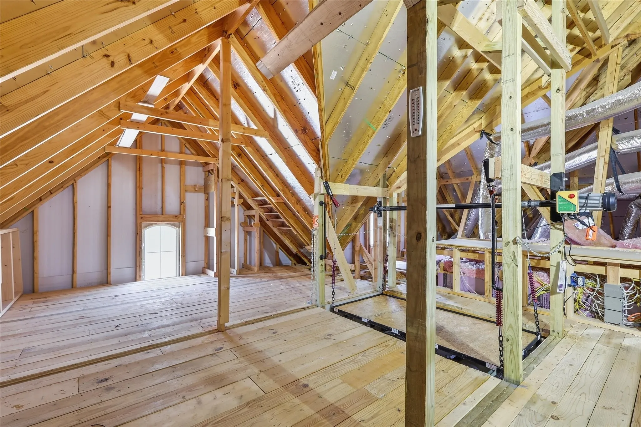 Unfinished attic space with exposed wooden rafters, a gabled roofline, a built-in window, and wood-plank flooring