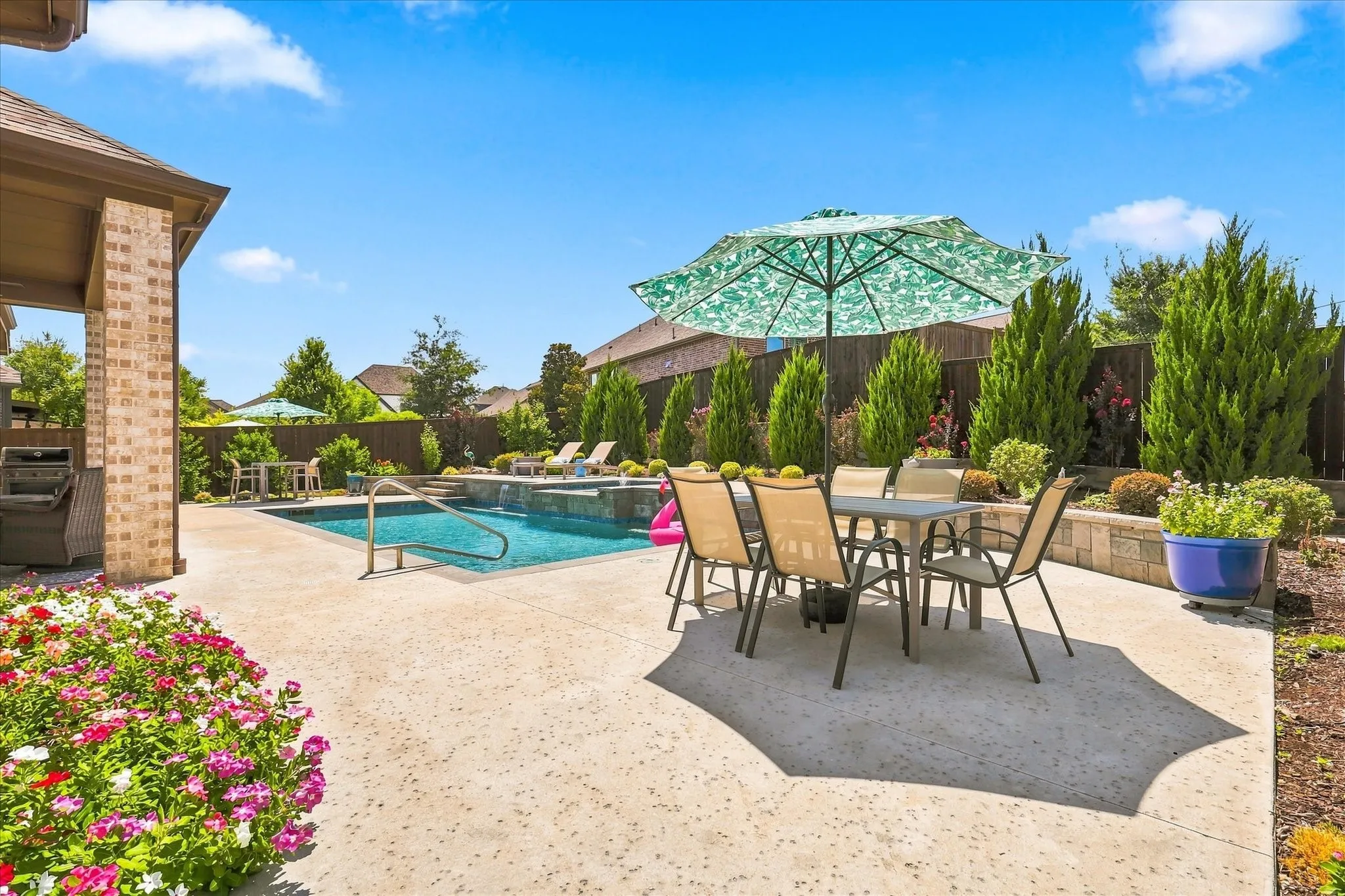 Expansive outdoor space featuring a swimming pool, concrete patio, brick columns, and manicured landscaping