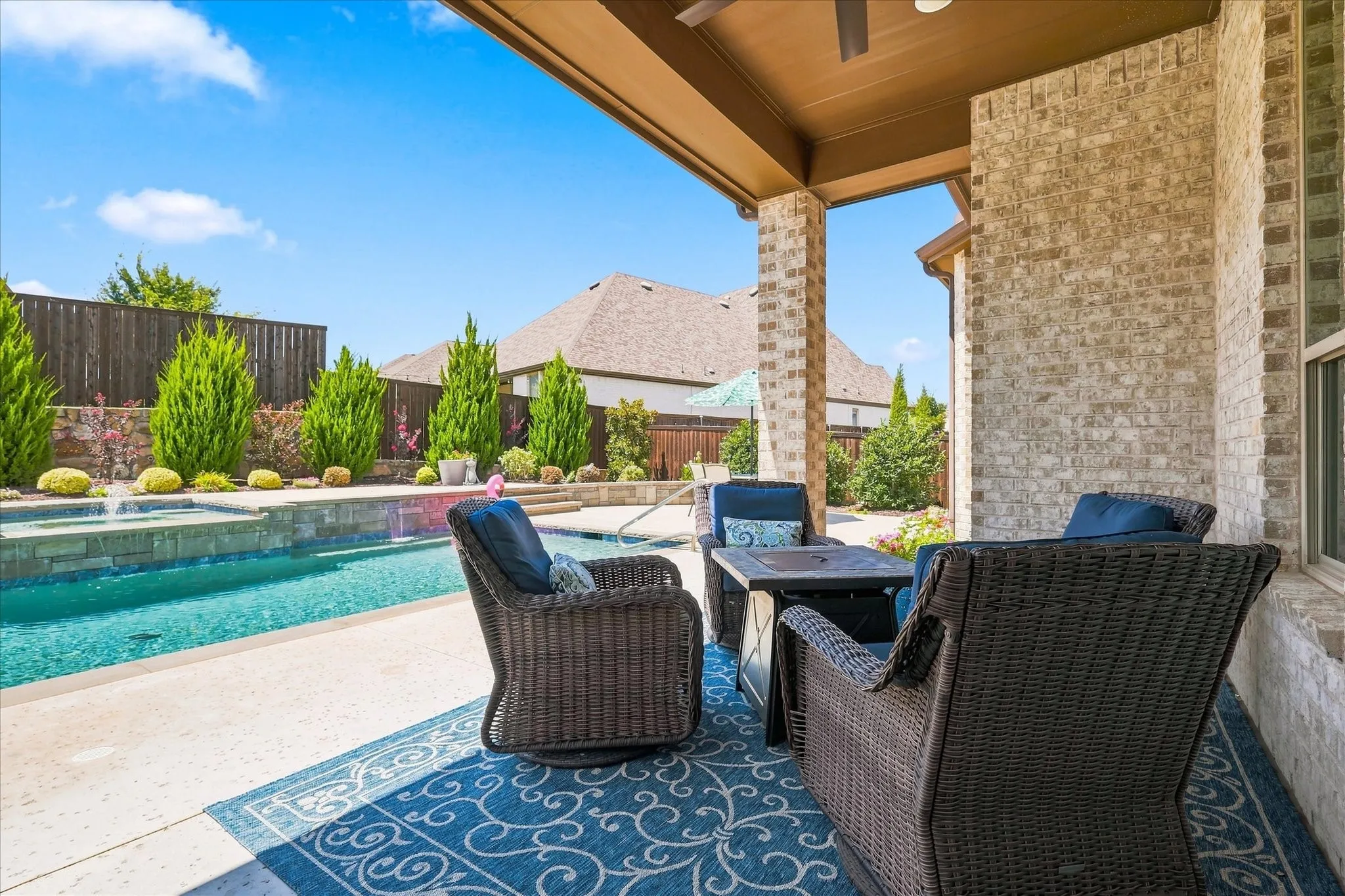 Covered patio with brick columns, an inground swimming pool with water features, and a landscaped perimeter