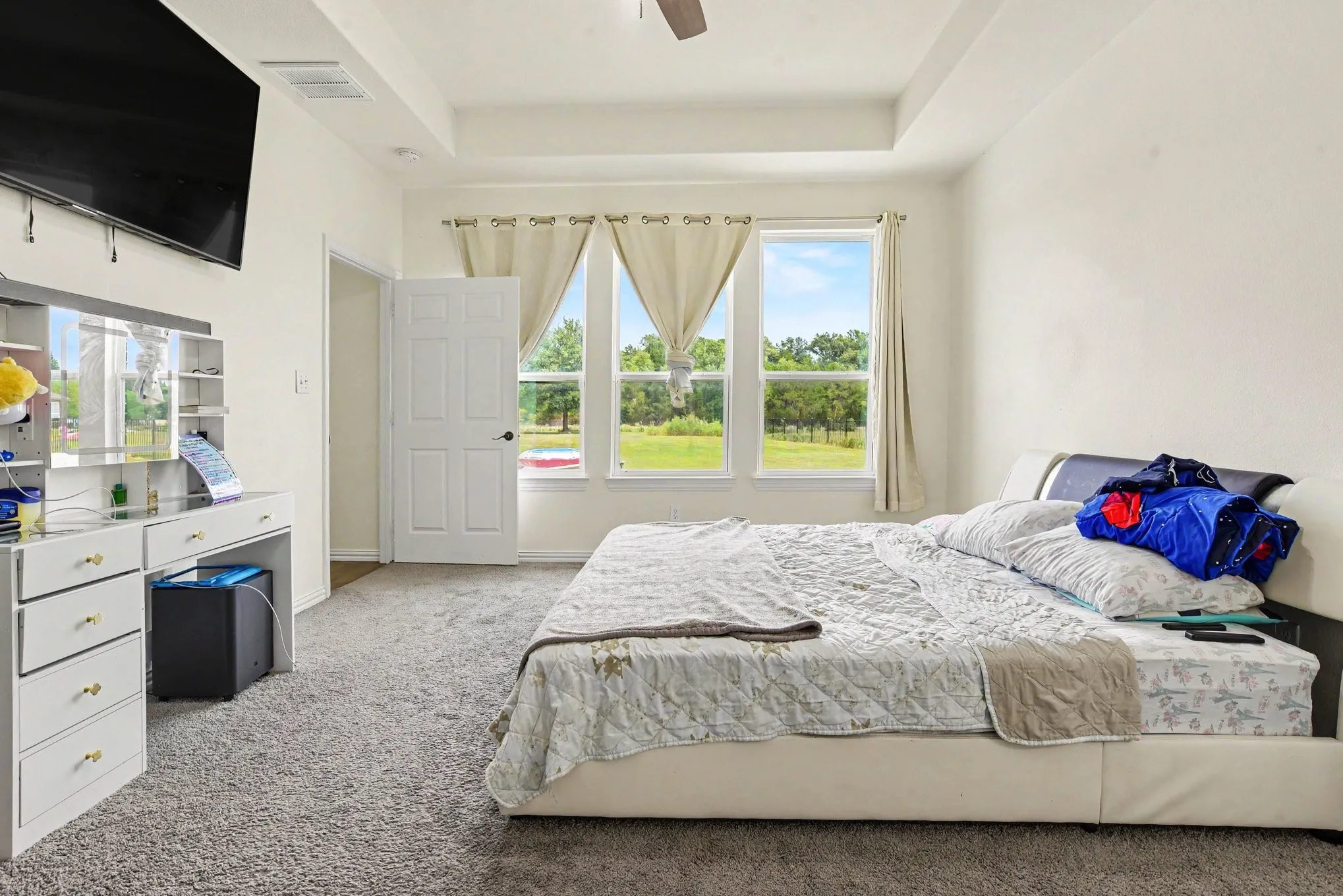 Spacious primary bedroom with expansive glass doors opening to manicured grounds, abundant natural light, carpeted flooring, and ceiling fan.