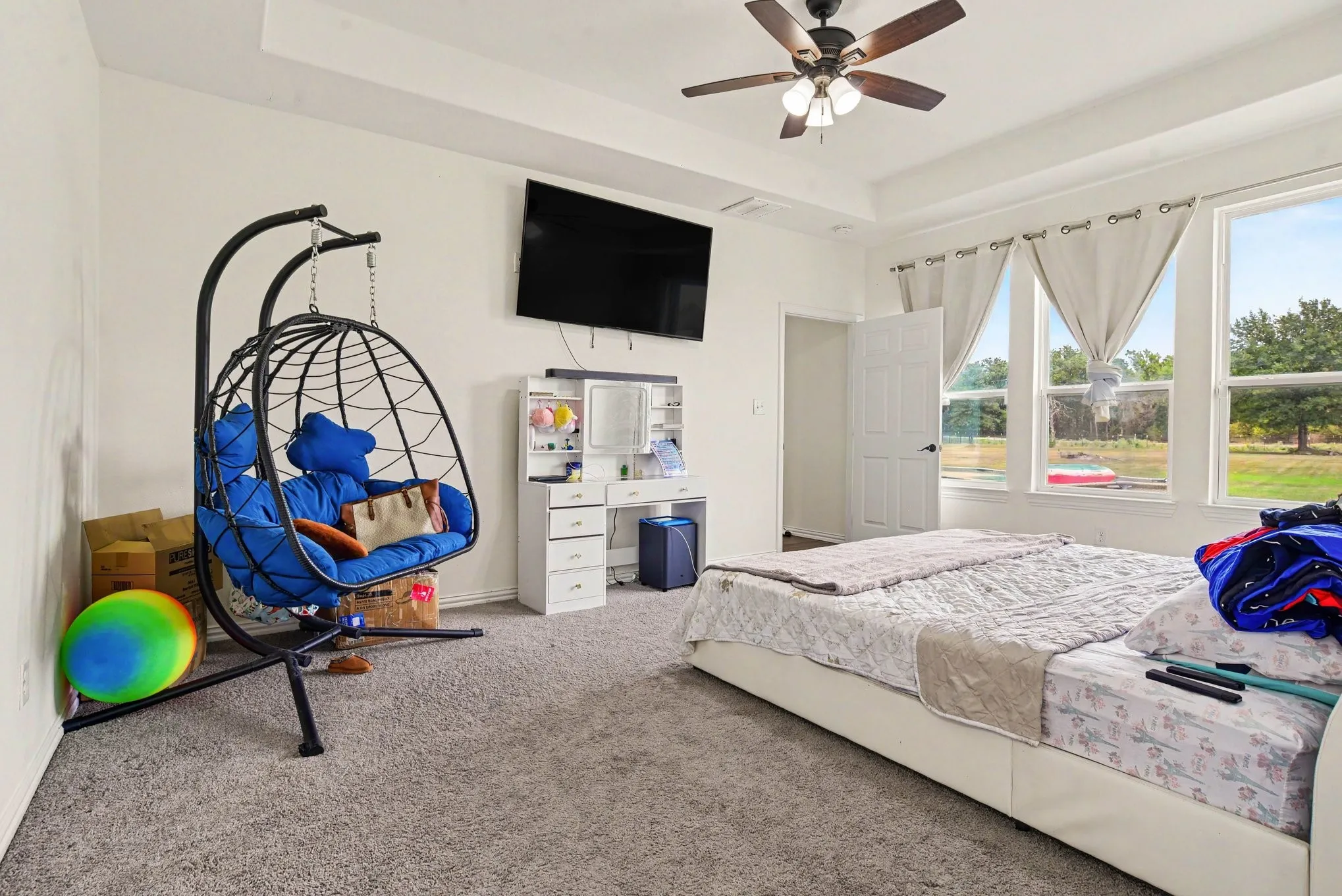 Tray ceiling, ceiling fan, white paneled door, three large windows, and carpet flooring
