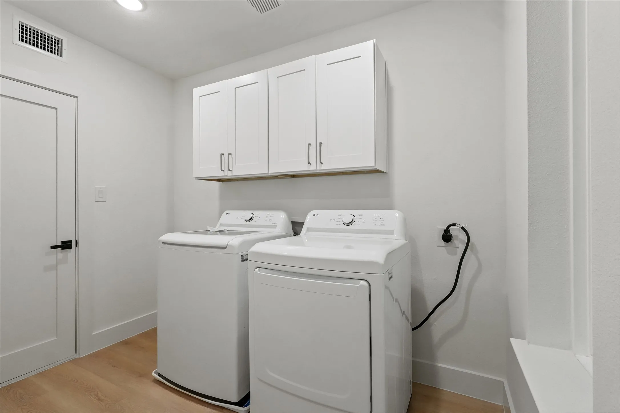 Laundry area with light wood-style flooring, washer and dryer, and cabinet space