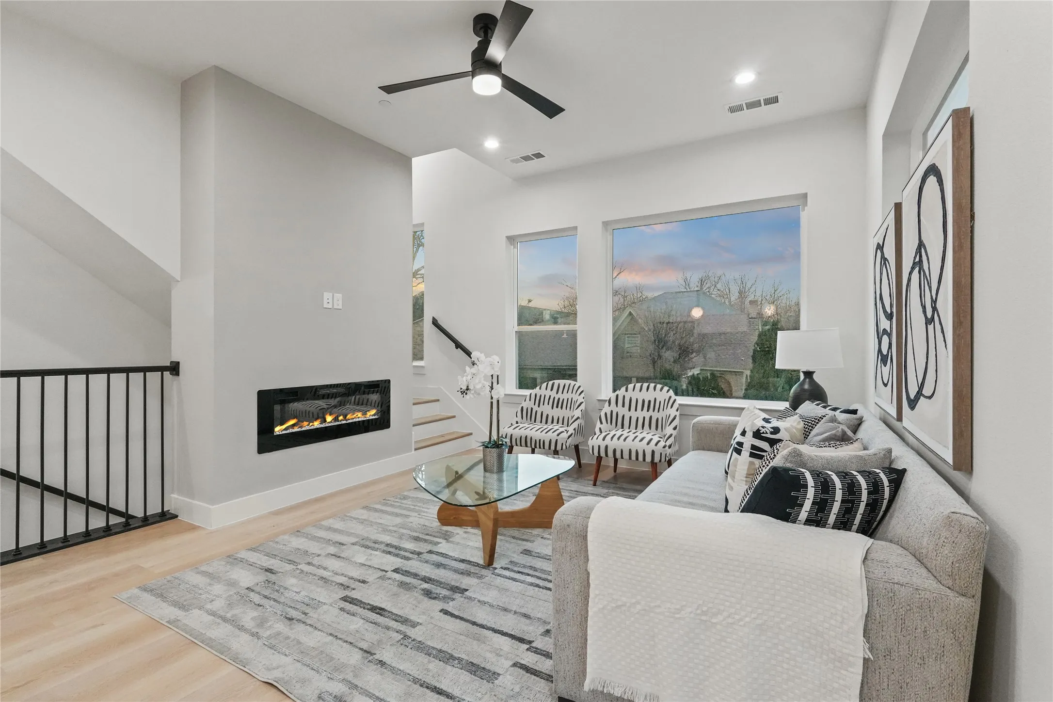 Living area with a glass covered fireplace, wood finished floors, ceiling fan, recessed lighting, and a high ceiling