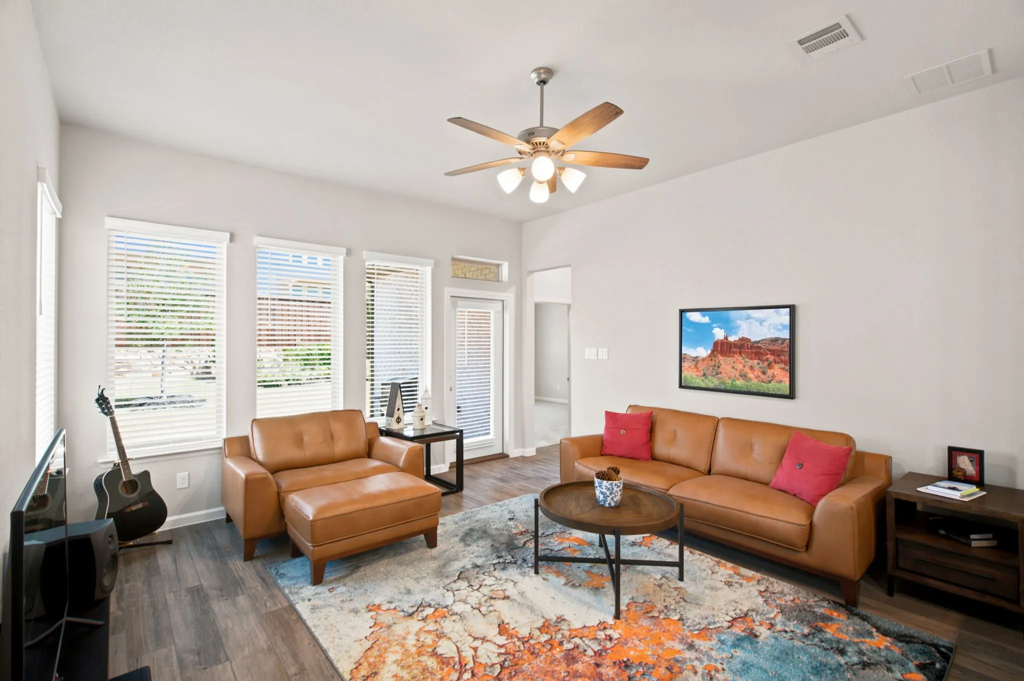Spacious living area featuring wood-finish flooring, multiple windows with blinds, and a ceiling fan with integrated lighting