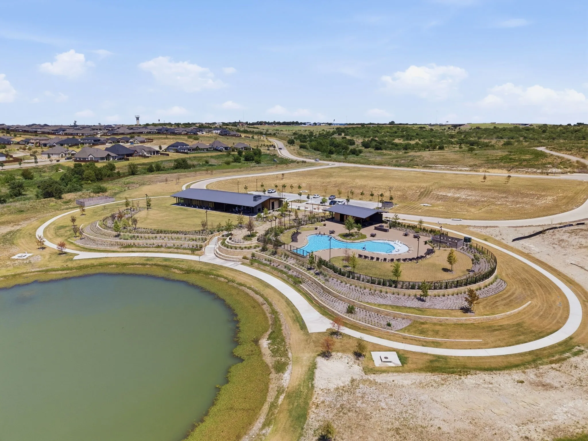 Community amenities featuring a resort-style pool, surrounding hardscaping, a large community building, a separate covered structure, and a walking path bordering a lake
