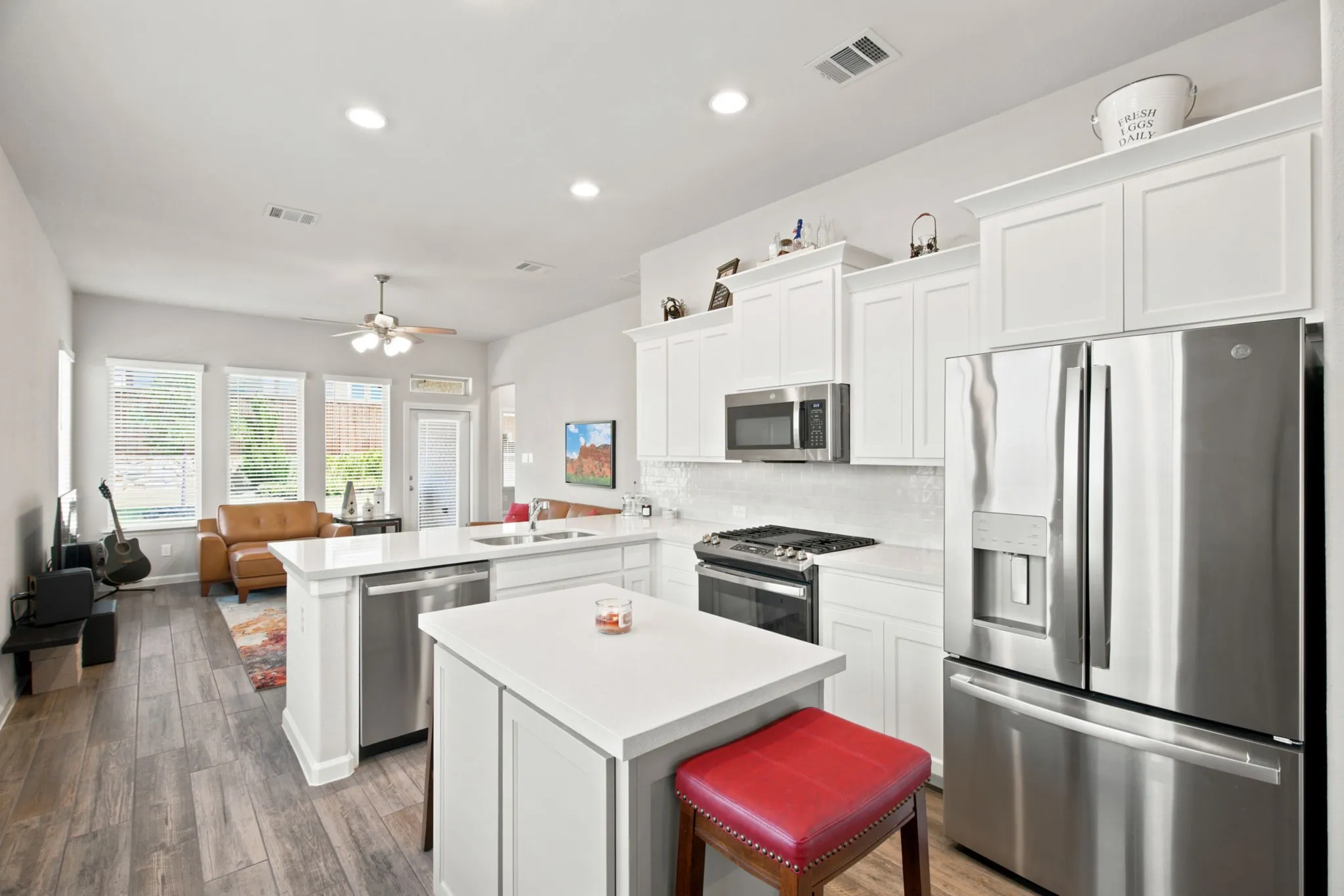 Open-concept kitchen with white cabinetry, stainless steel appliances, and wood-finish flooring