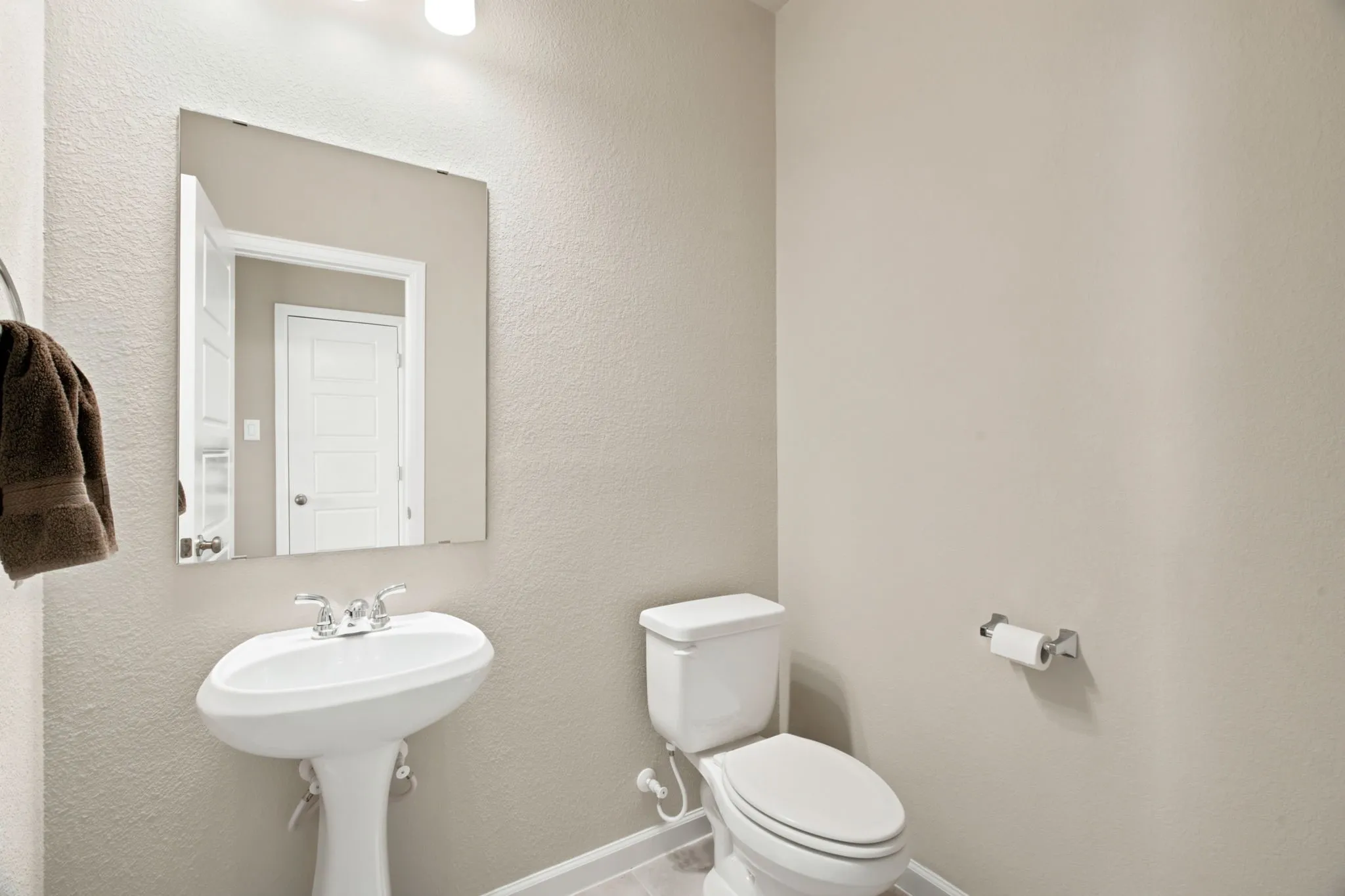 Pedestal sink with chrome faucet, wall-mounted mirror, and white toilet