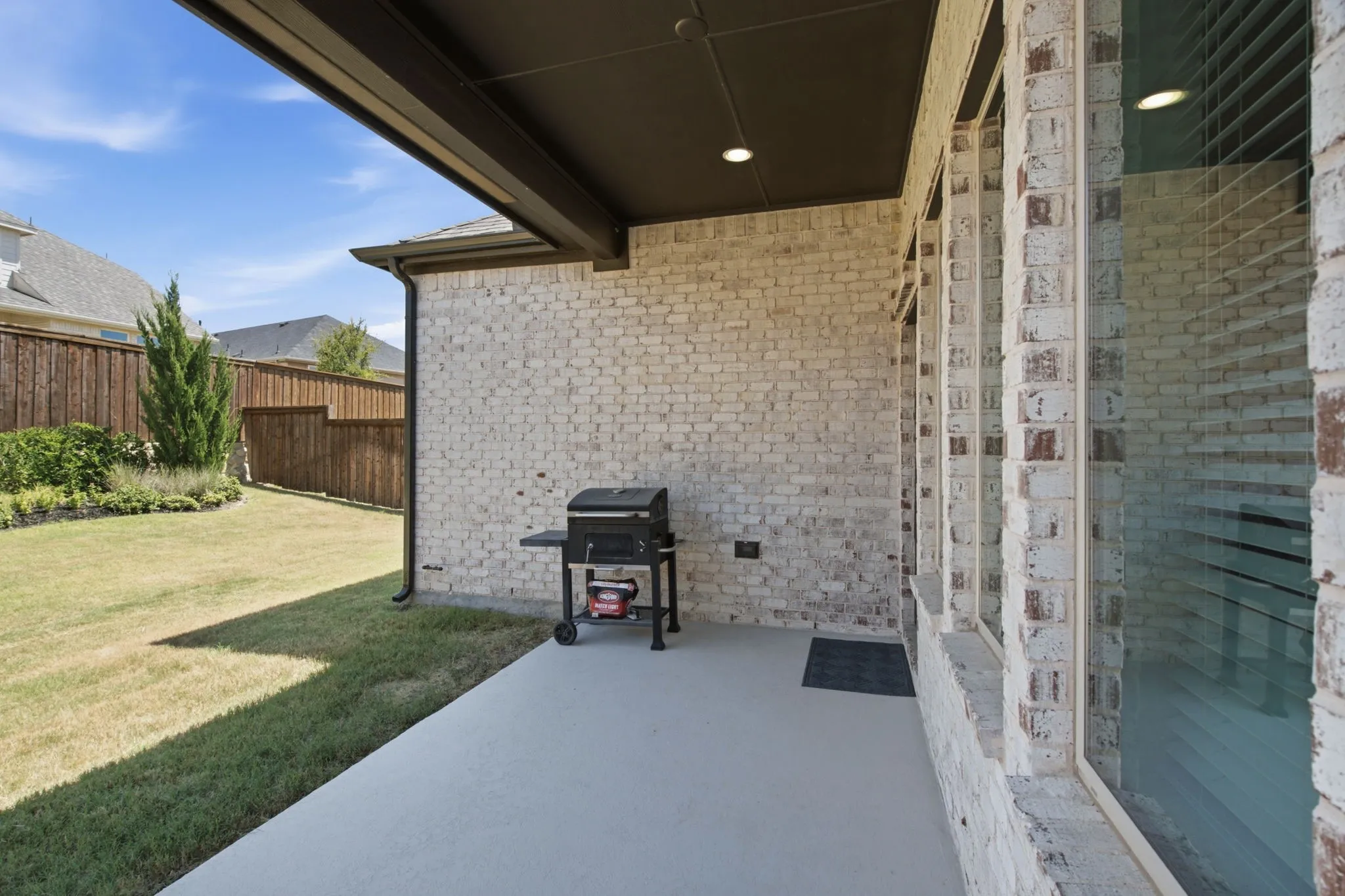 Covered patio with a concrete surface, white brick exterior, and a manicured lawn