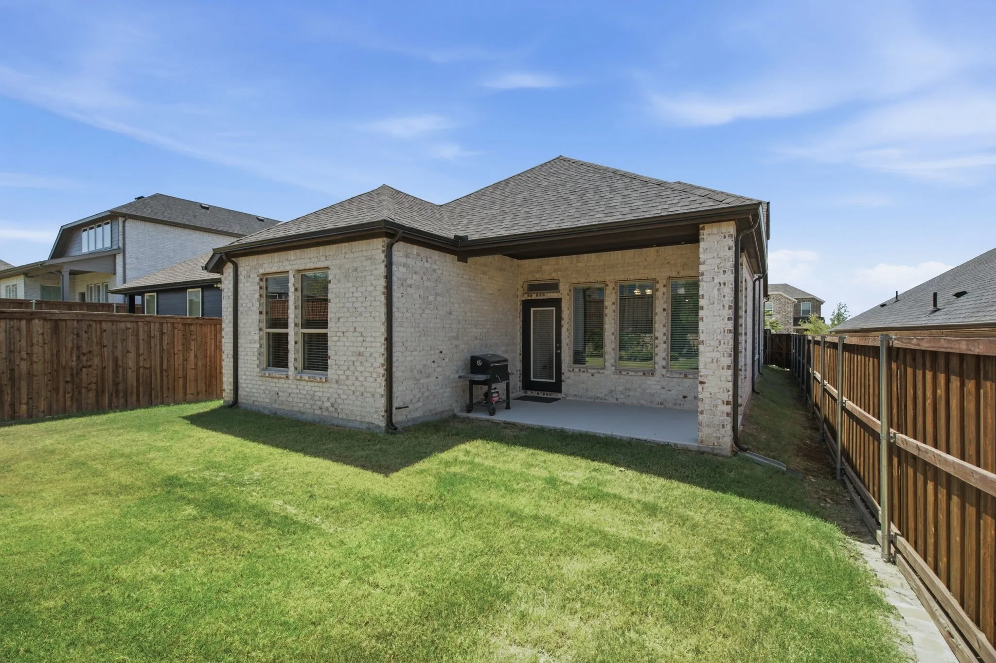 Expansive backyard featuring a manicured lawn, brick exterior, covered patio, and privacy fencing