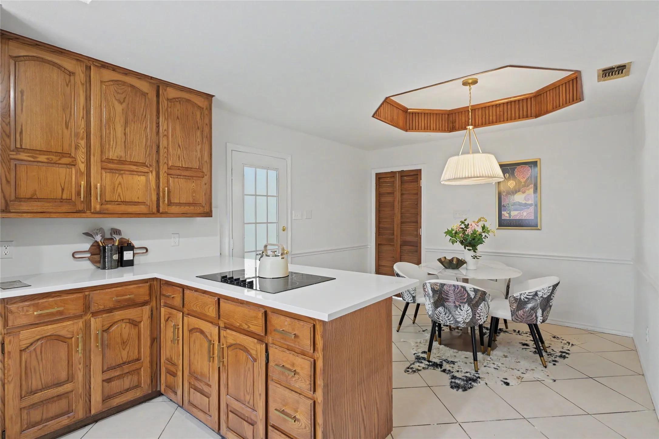 Wood cabinetry with gold-tone hardware, white countertops, built-in cooktop, and a white tile flooring