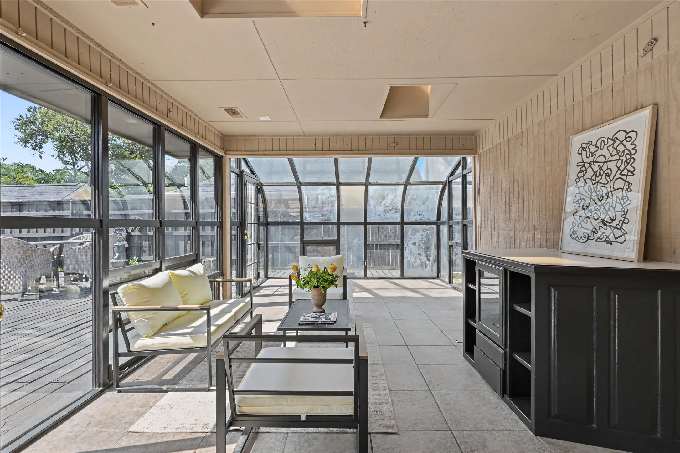 Sunroom with a tile floor, extensive window panels, and a built-in dark wood-finish cabinet with open shelving
