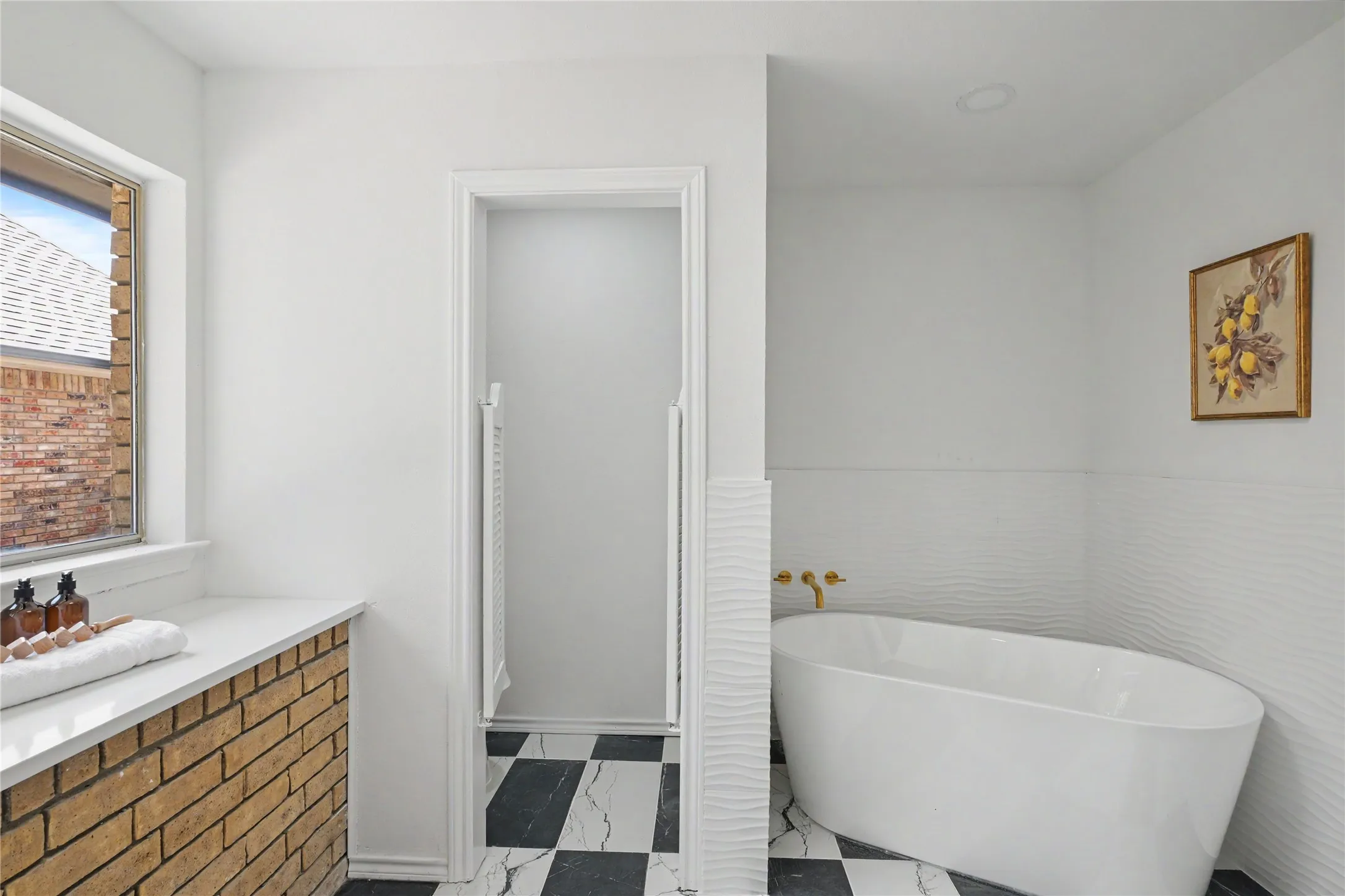 Freestanding soaking tub with wall-mounted brass fixtures, black and white checkered floor tile, and a brick-front vanity with a white countertop