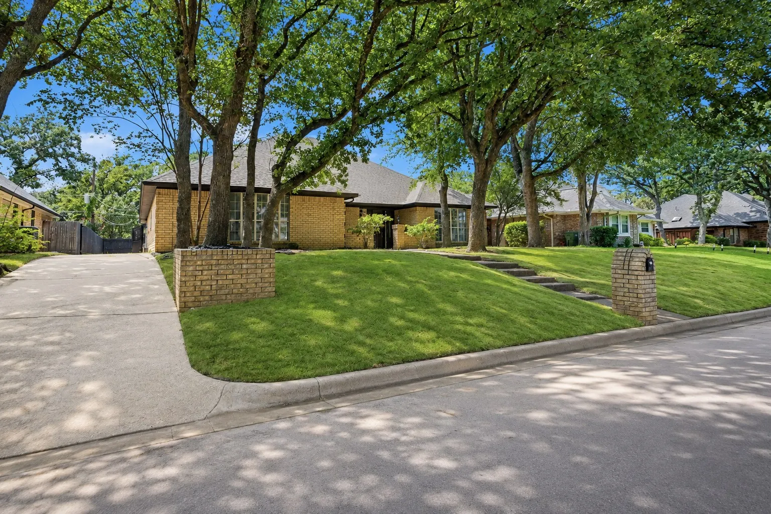 Brick exterior residence with a concrete driveway, mature trees, tiered lawn, and a brick mailbox