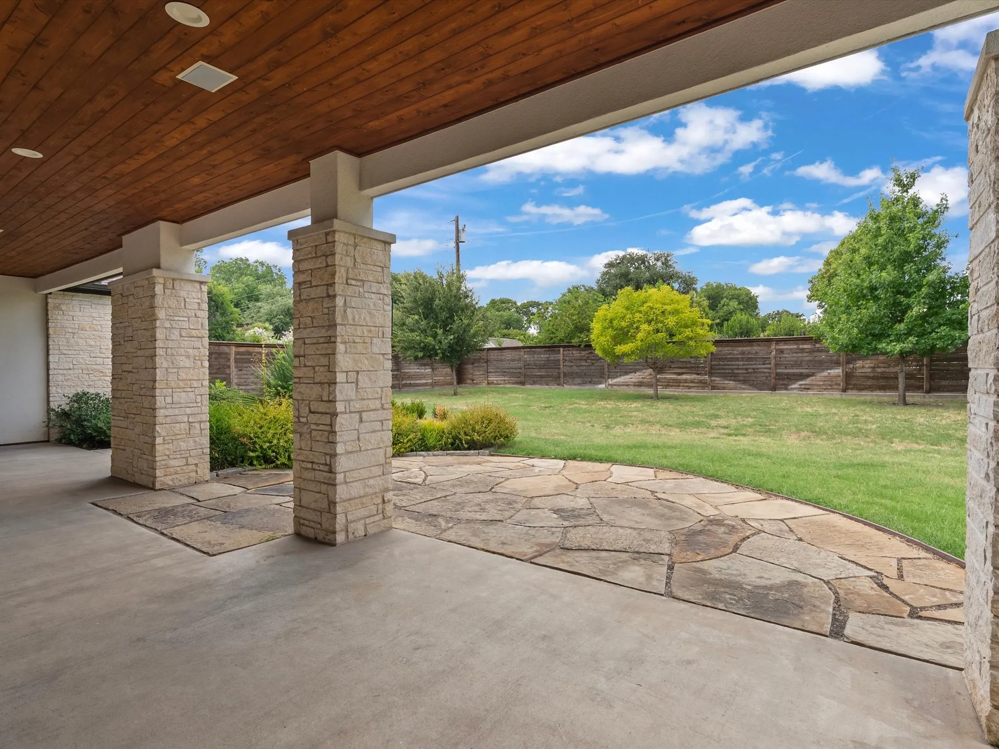 Covered patio with a wood-paneled ceiling, recessed lighting, and stone support columns