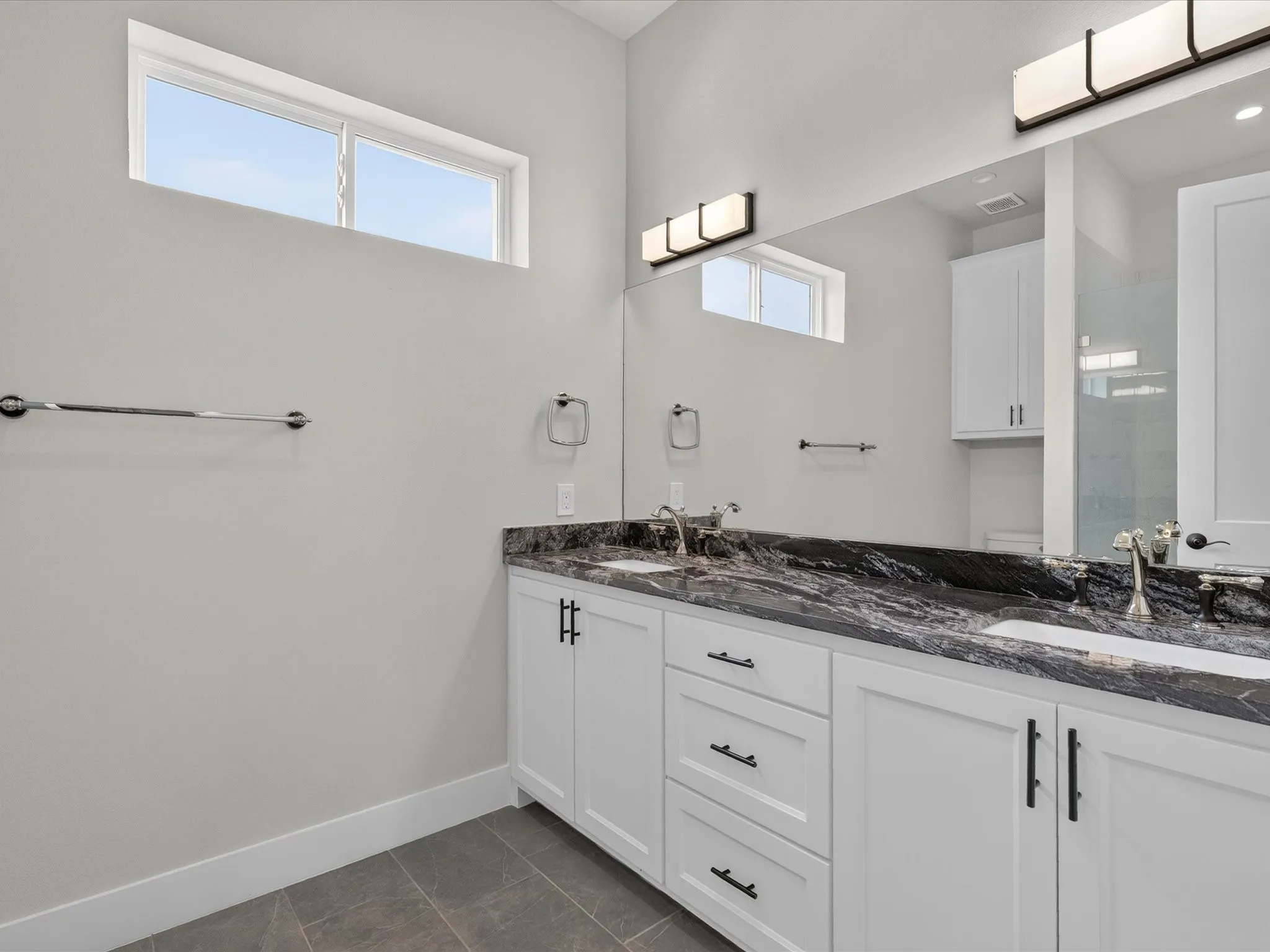 Double vanity featuring white cabinetry, dark stone countertop, undermount sinks, and wall-mounted light fixtures