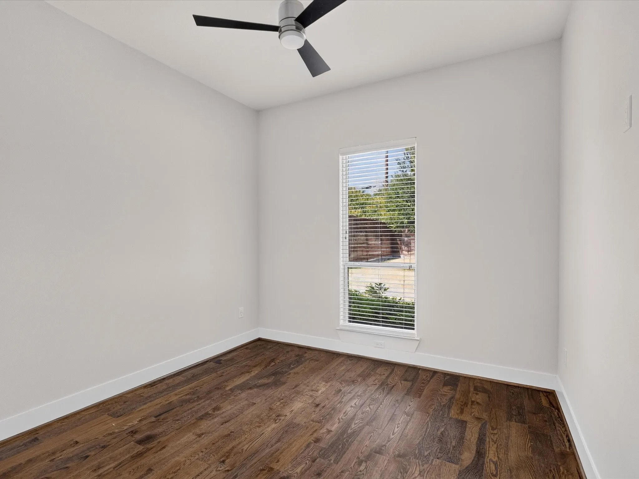 Light-filled room featuring wood-finish flooring, a window with blinds, and a ceiling fan