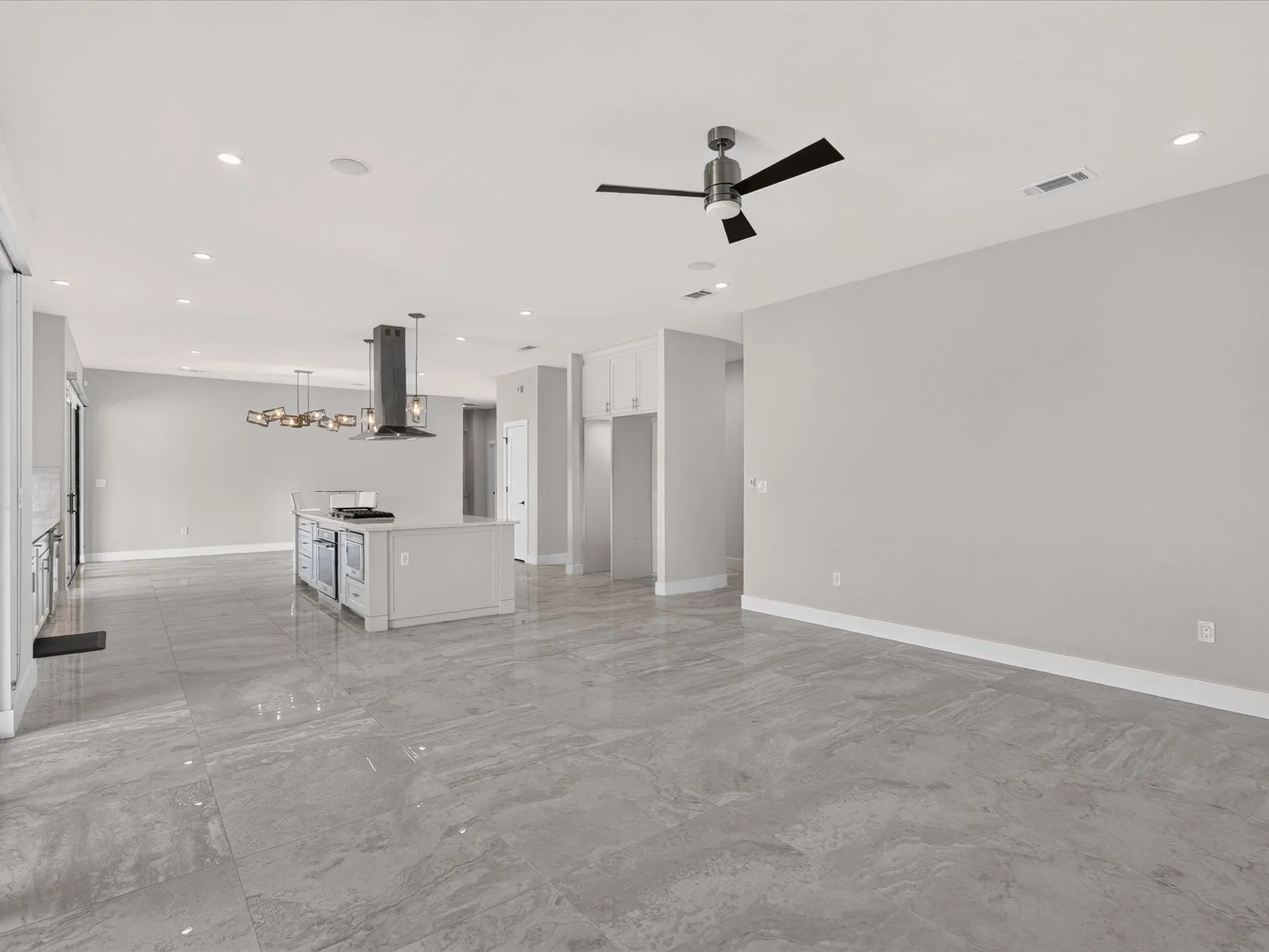 Expansive open-concept living area featuring large format tile flooring, a kitchen island with built-in appliances, a contemporary chandelier, recessed lighting, and a modern ceiling fan