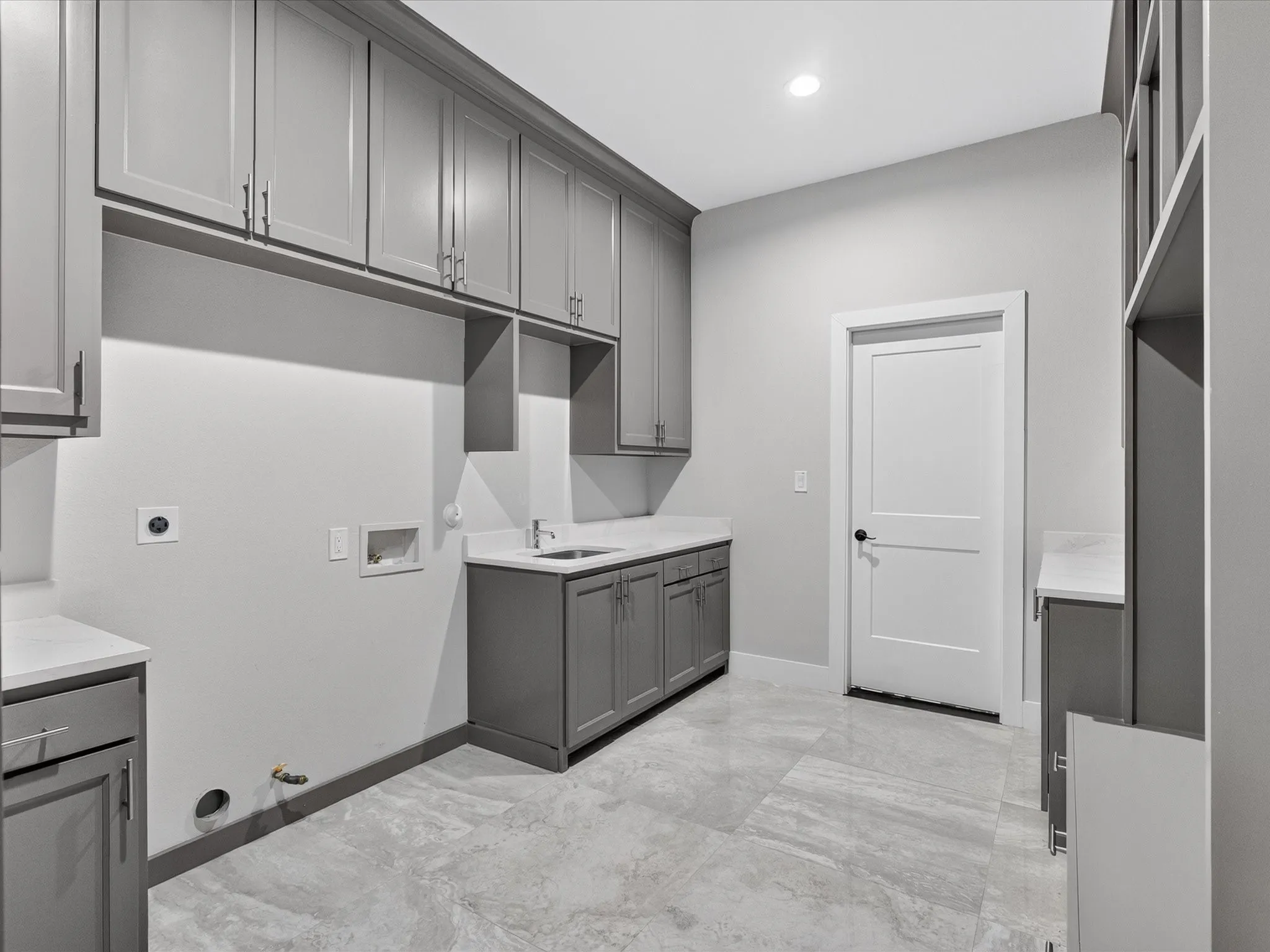 Utility area with gray cabinetry, light-toned countertops, a built-in sink, and light-toned tile flooring