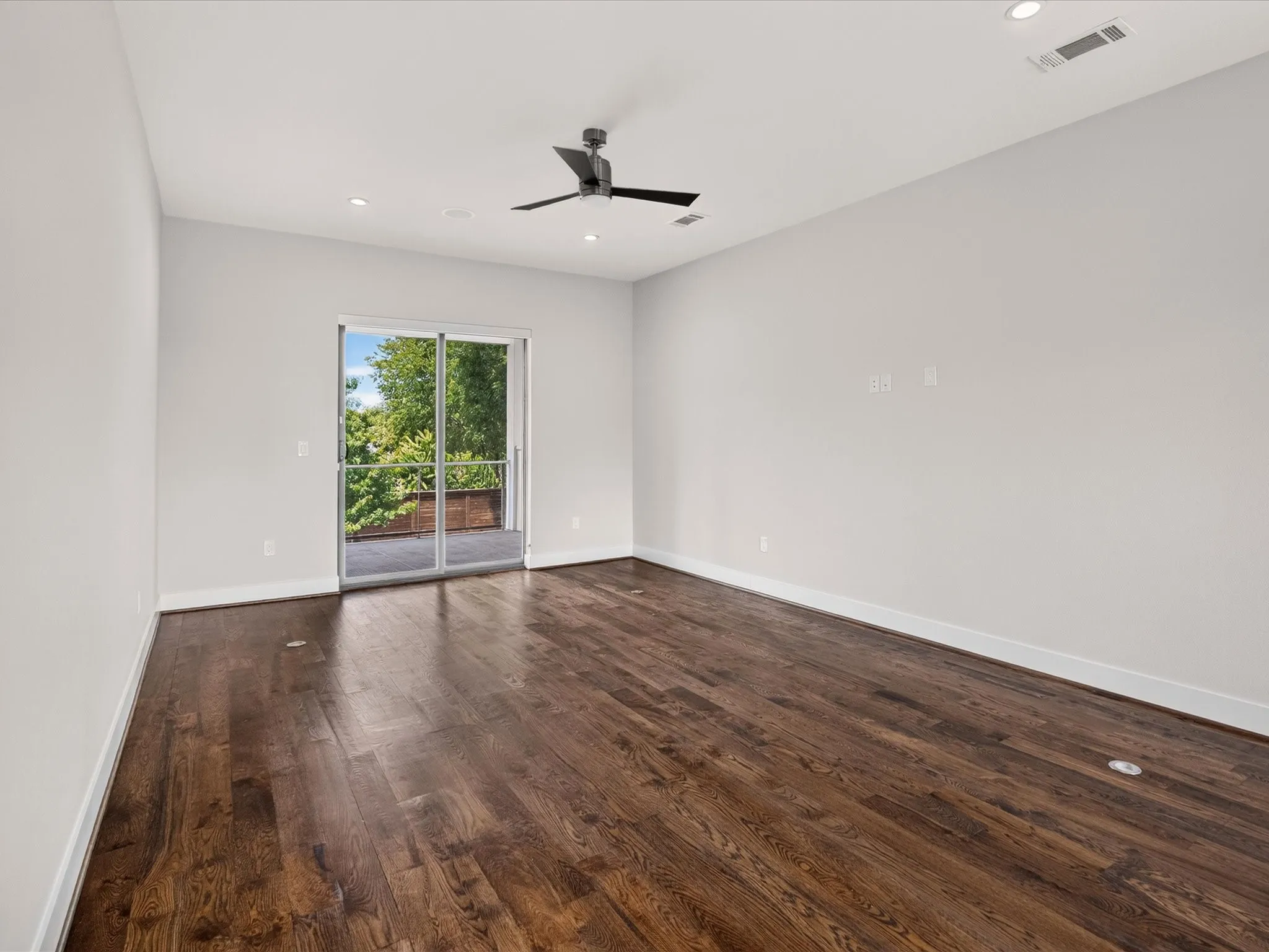 Dark wood-finish flooring, white walls, recessed ceiling lighting, ceiling fan, and sliding glass doors to outdoor area