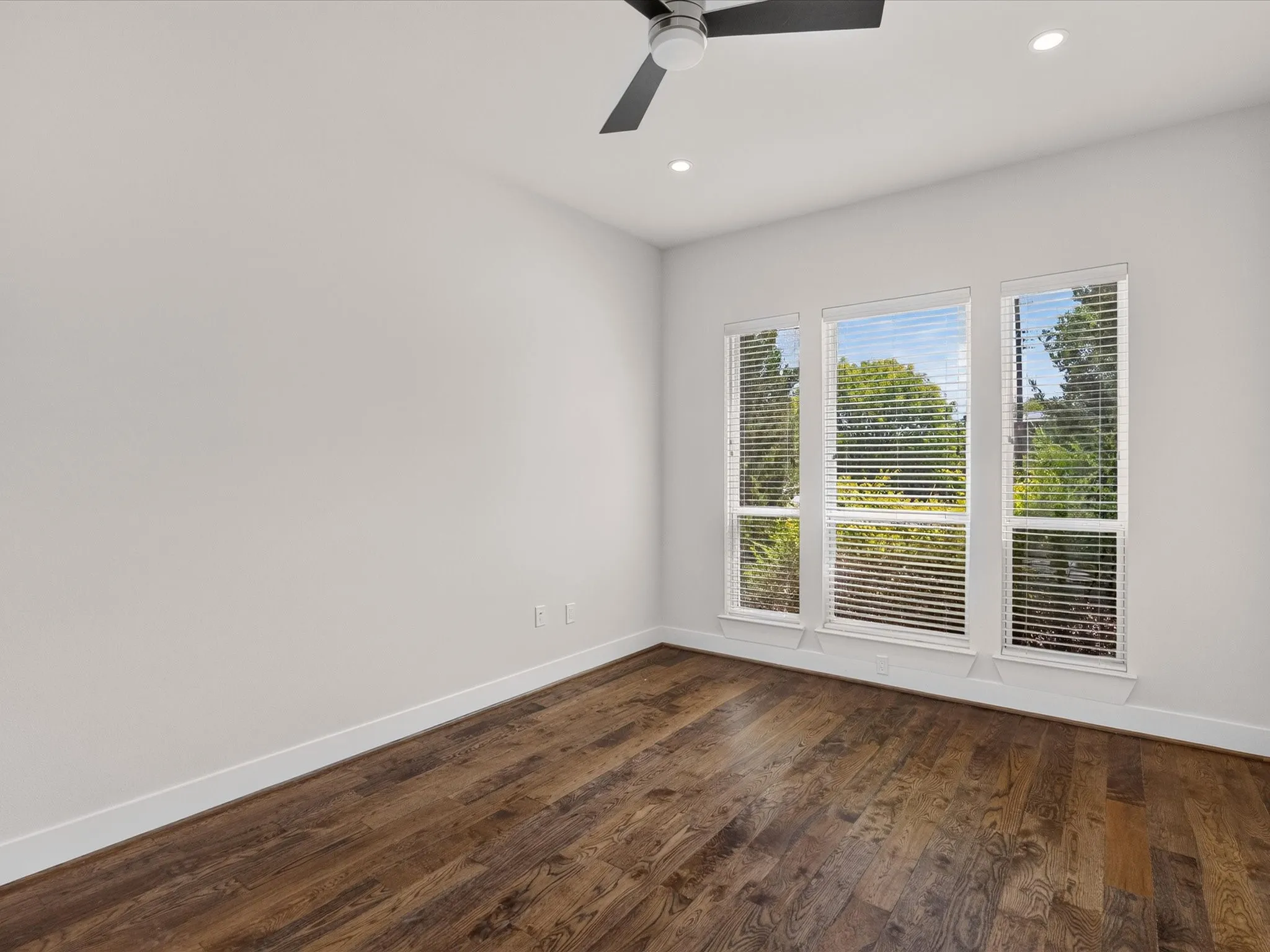 Wood-finish flooring, white walls, triple window configuration, recessed lighting, and a ceiling fan