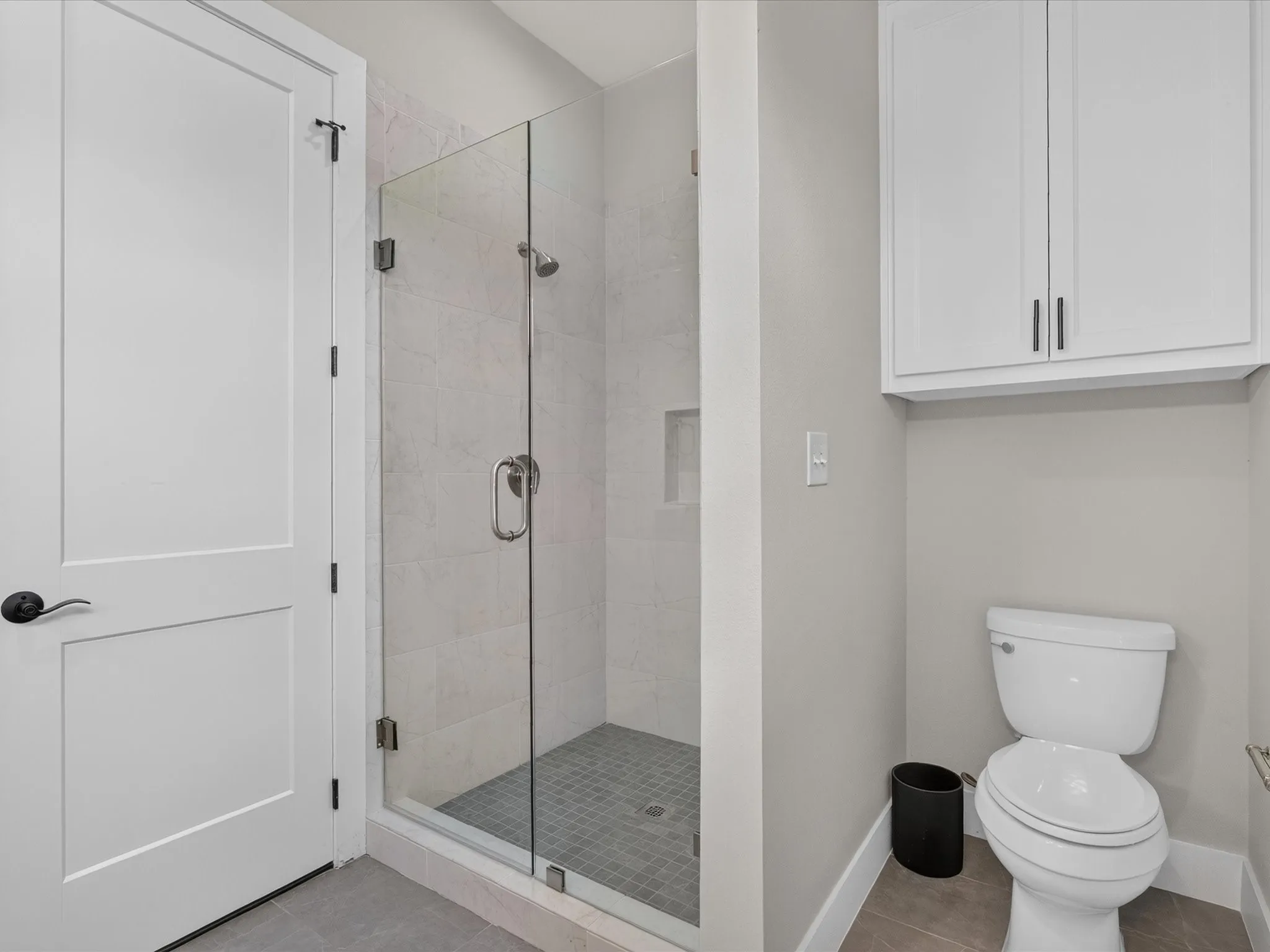 Full glass shower enclosure with tile surround, built-in shower niche, overhead cabinetry, and a panel-style door