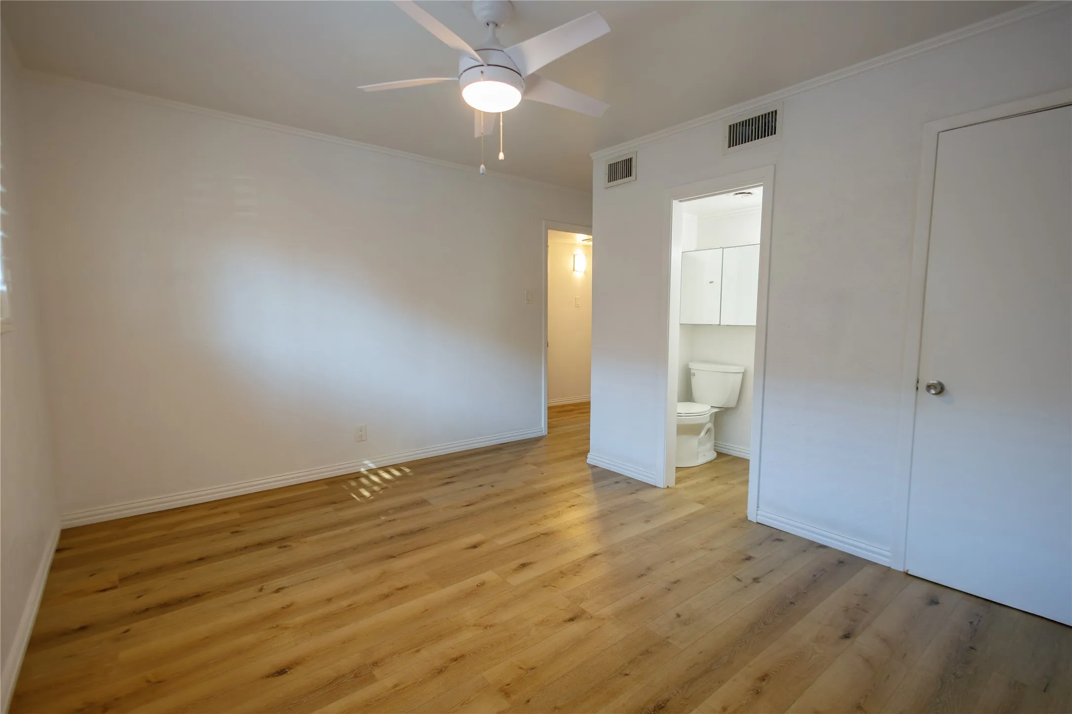 Wood-finish flooring throughout, bright white walls, and a ceiling fan with integrated lighting