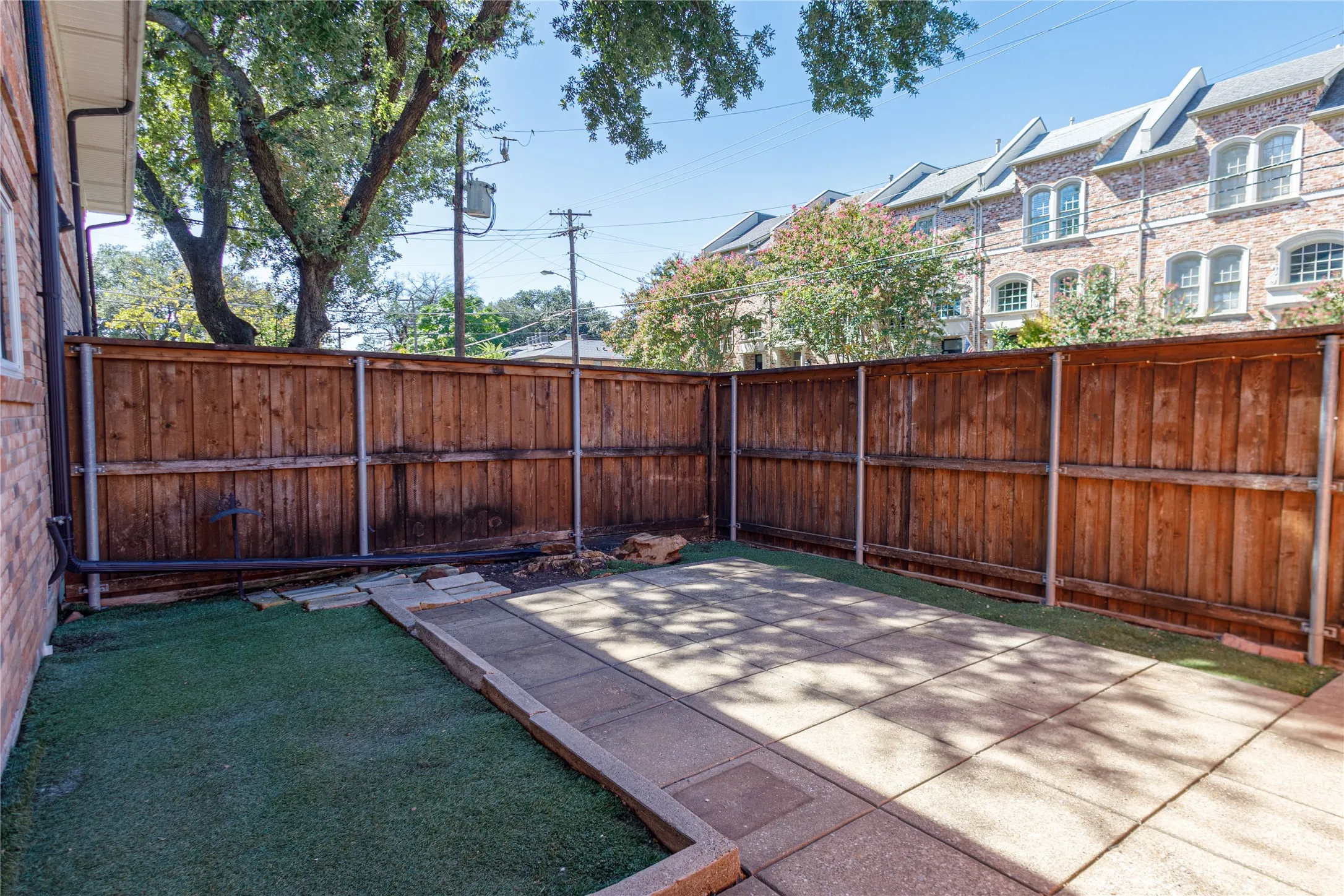 Enclosed outdoor area featuring a wood fence, artificial turf, and paver patio