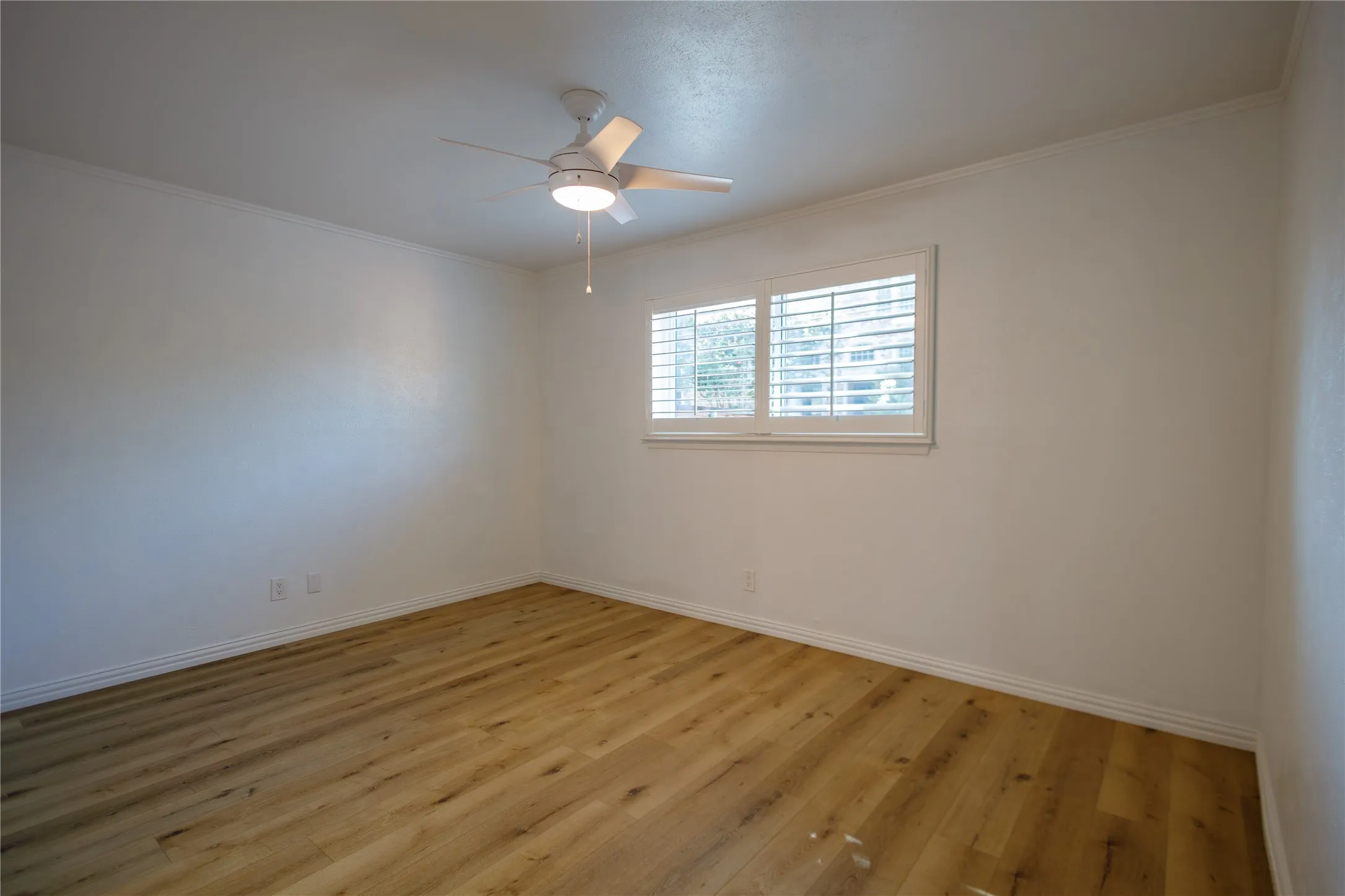 Wood-finish flooring, white plantation shutters, and a ceiling fan with integrated lighting